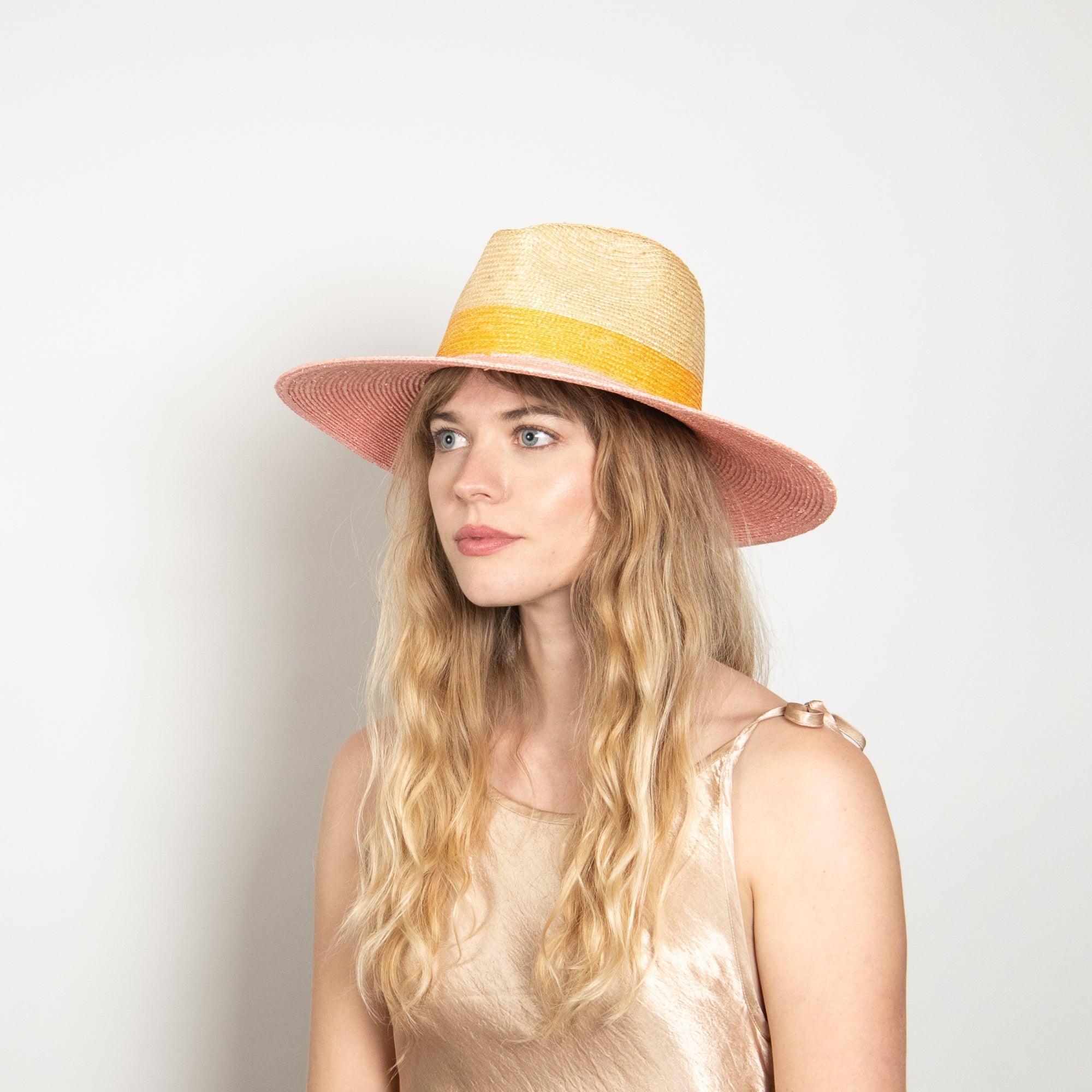 Woman wearing a straw hat with a yellow band on a plain background