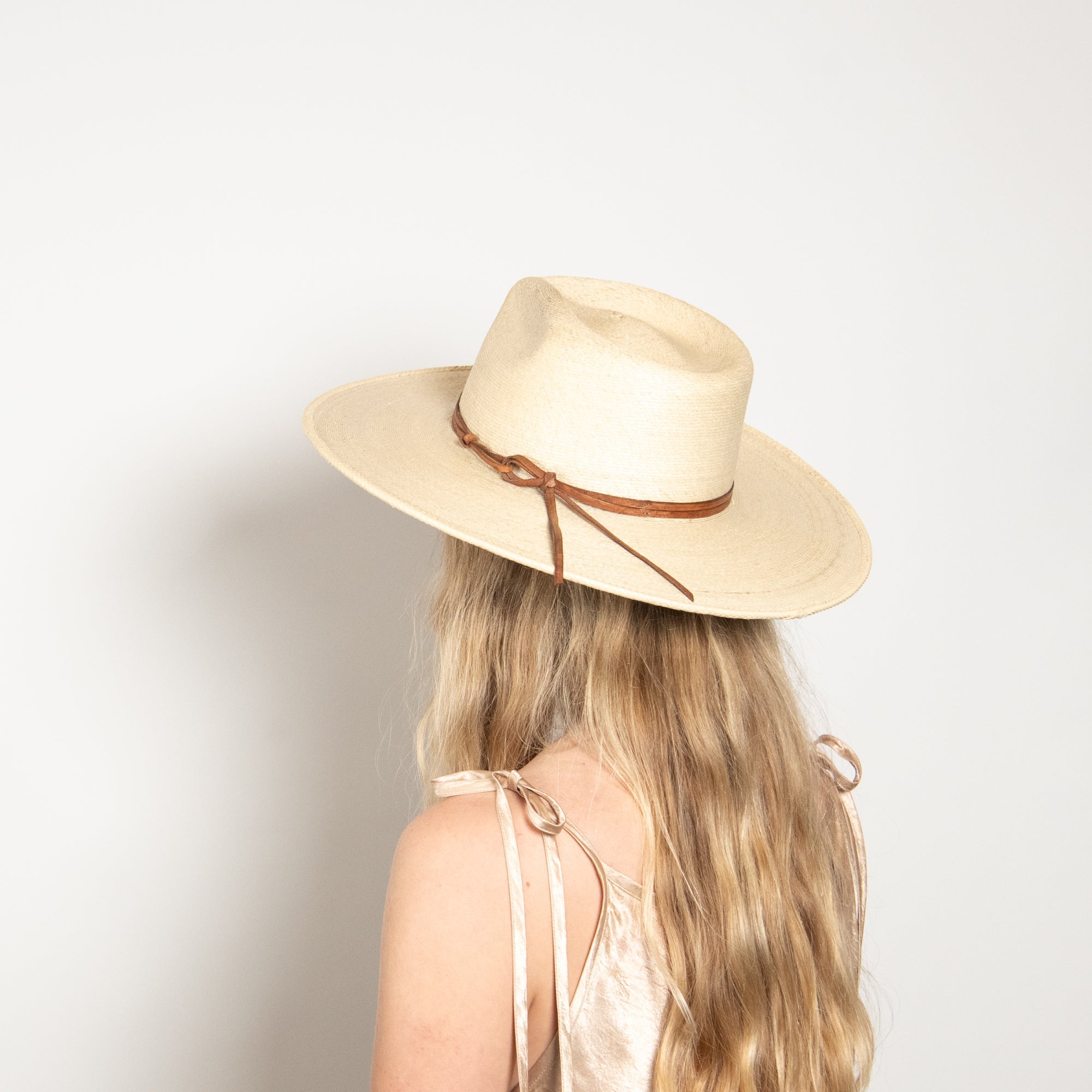 Person wearing a beige fedora hat with a brown ribbon on a light background