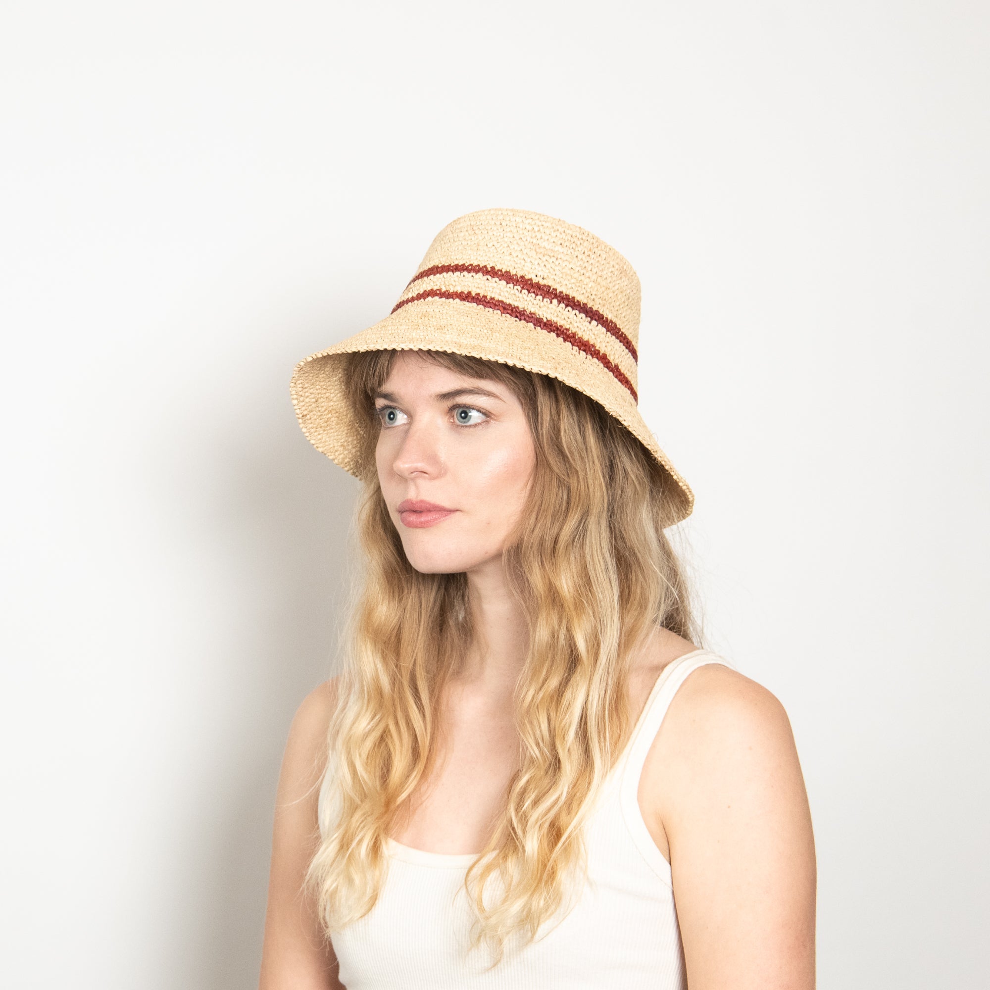 Woman wearing a straw hat with a red band against a plain background