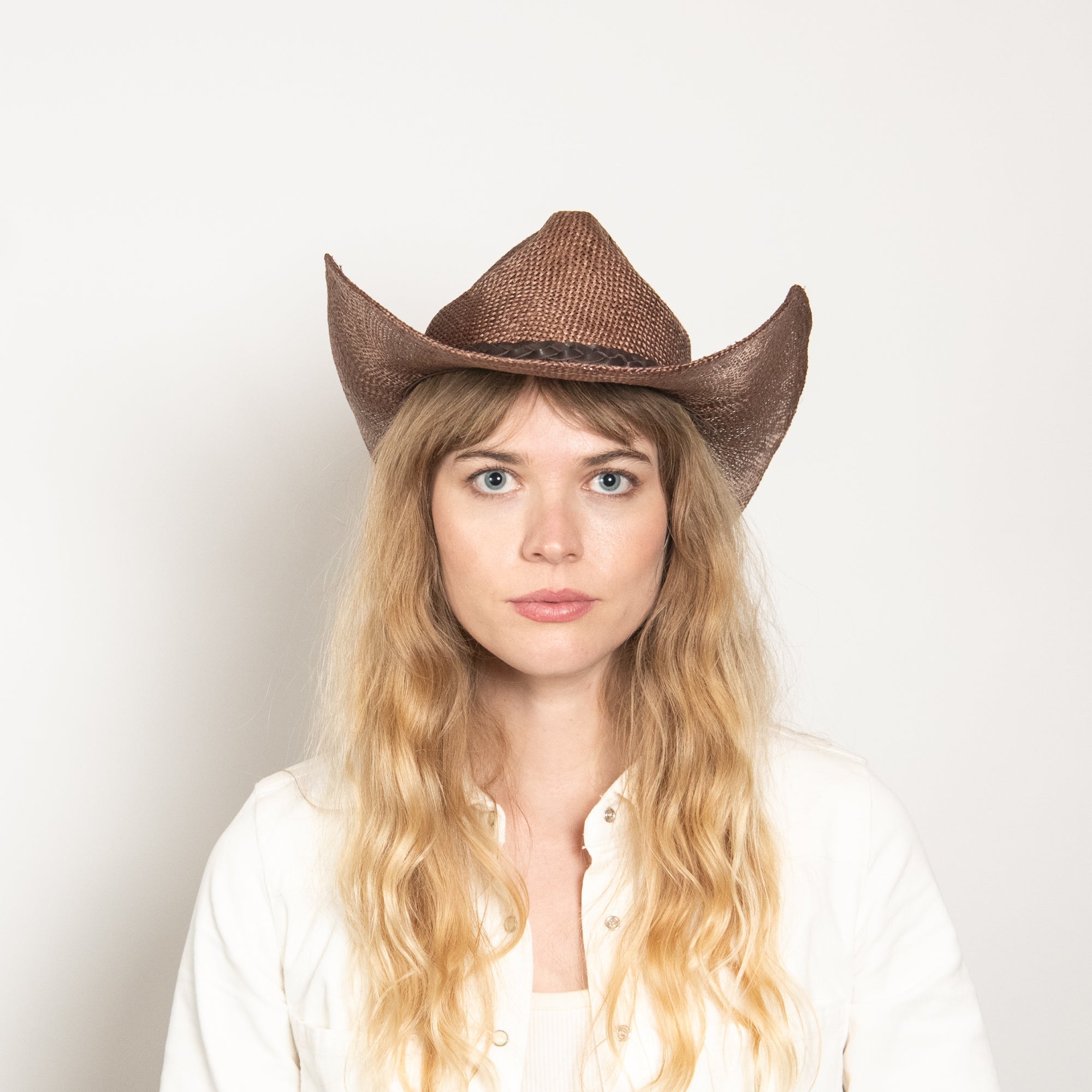 Person wearing a brown cowboy hat against a plain background