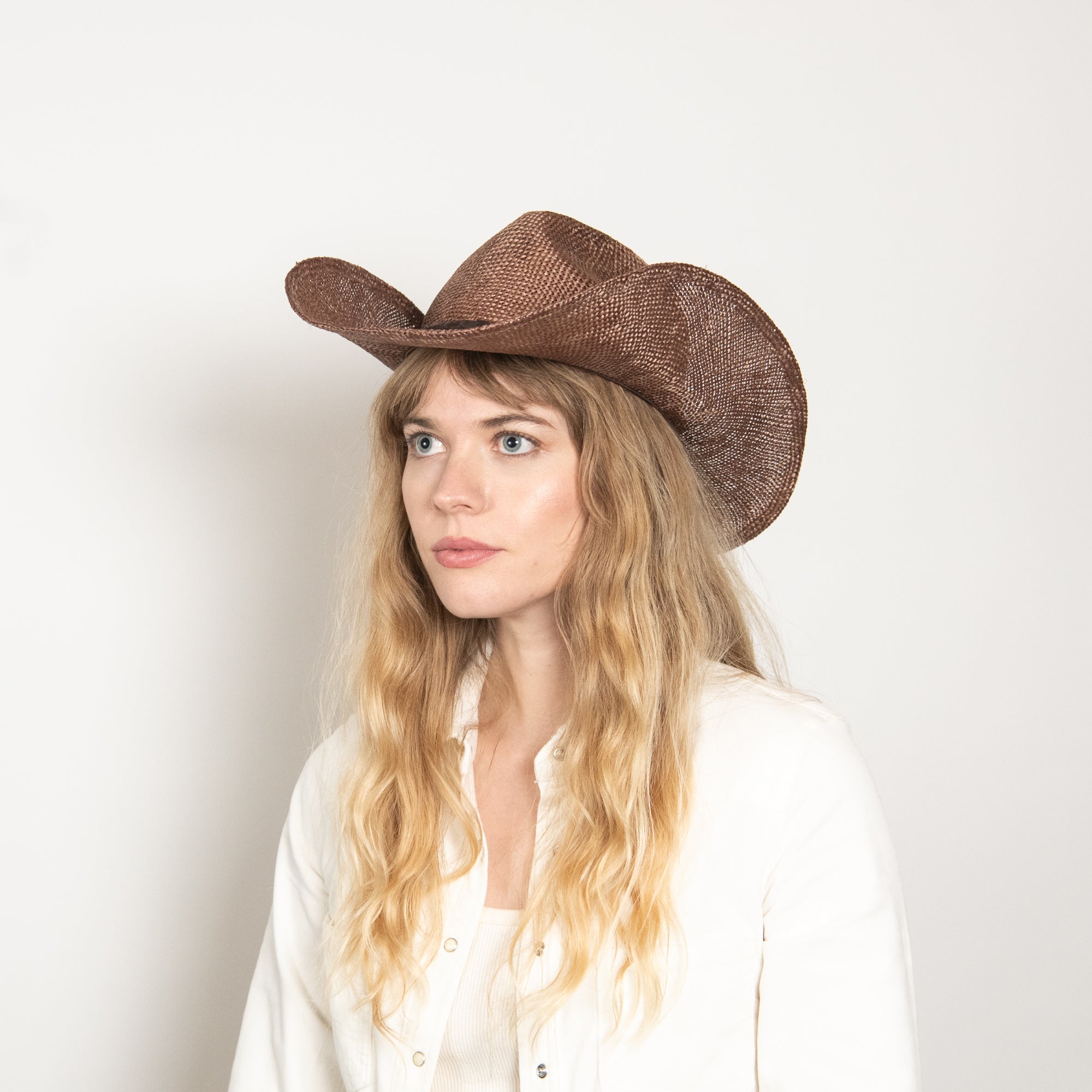 Woman wearing a brown cowboy hat against a plain background
