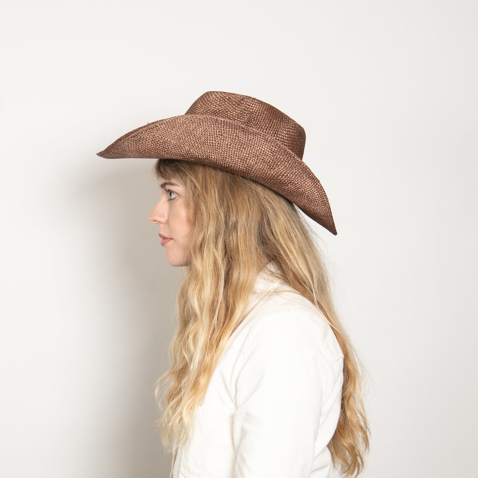Woman wearing a brown cowboy hat against a plain background