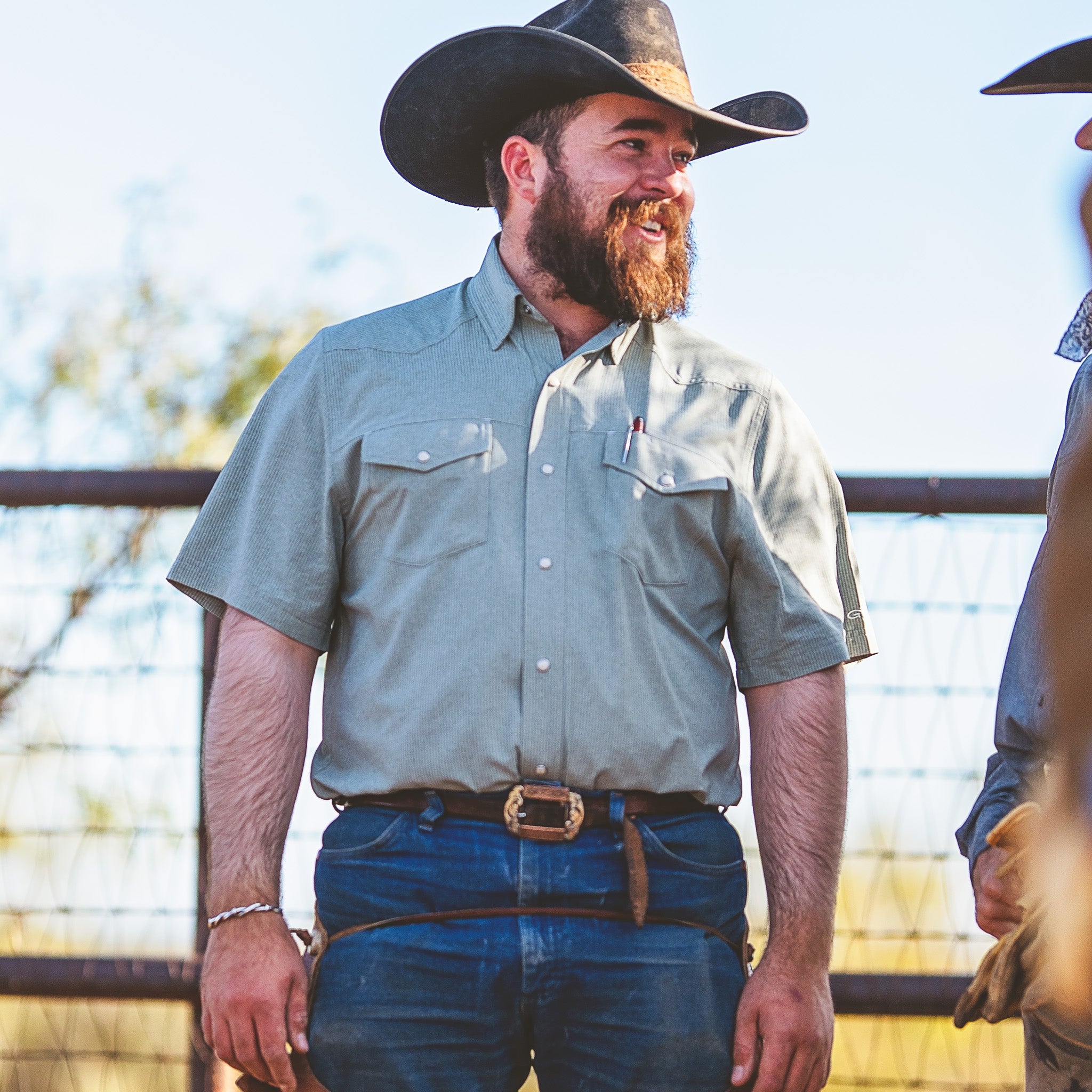 Man wearing a cowboy hat and light blue shirt standing outdoors with a blurred background