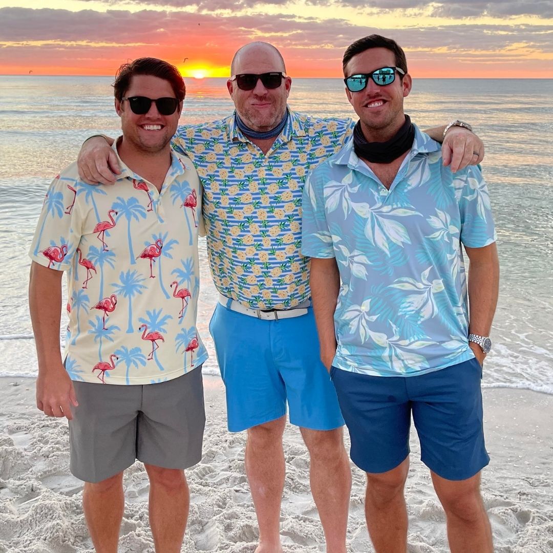 Three men posing on a beach with a sunset in the background