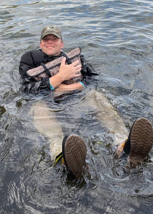 Person in waders holding a large fish in water