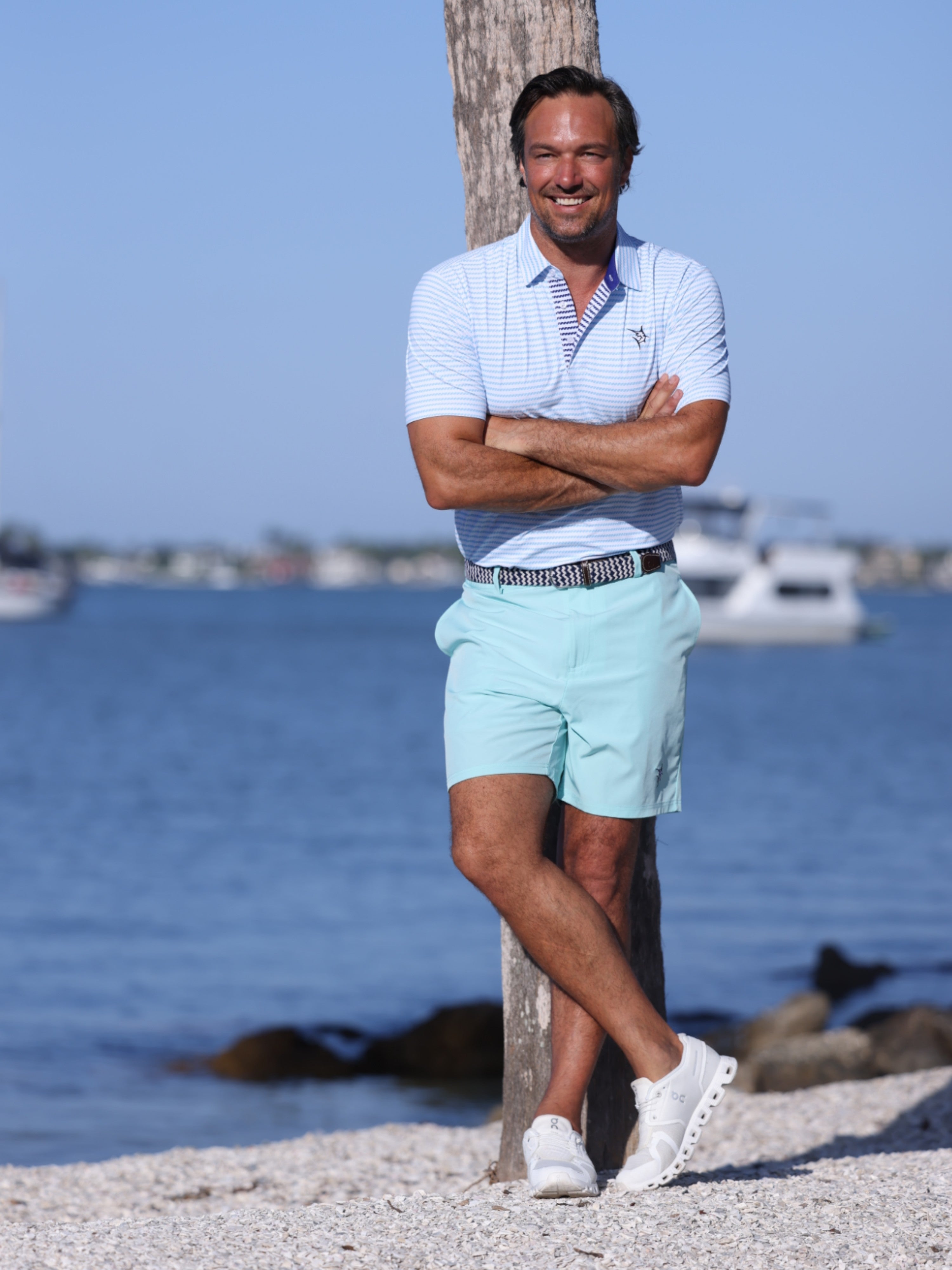 Man standing by a body of water wearing a light blue polo shirt and shorts.
