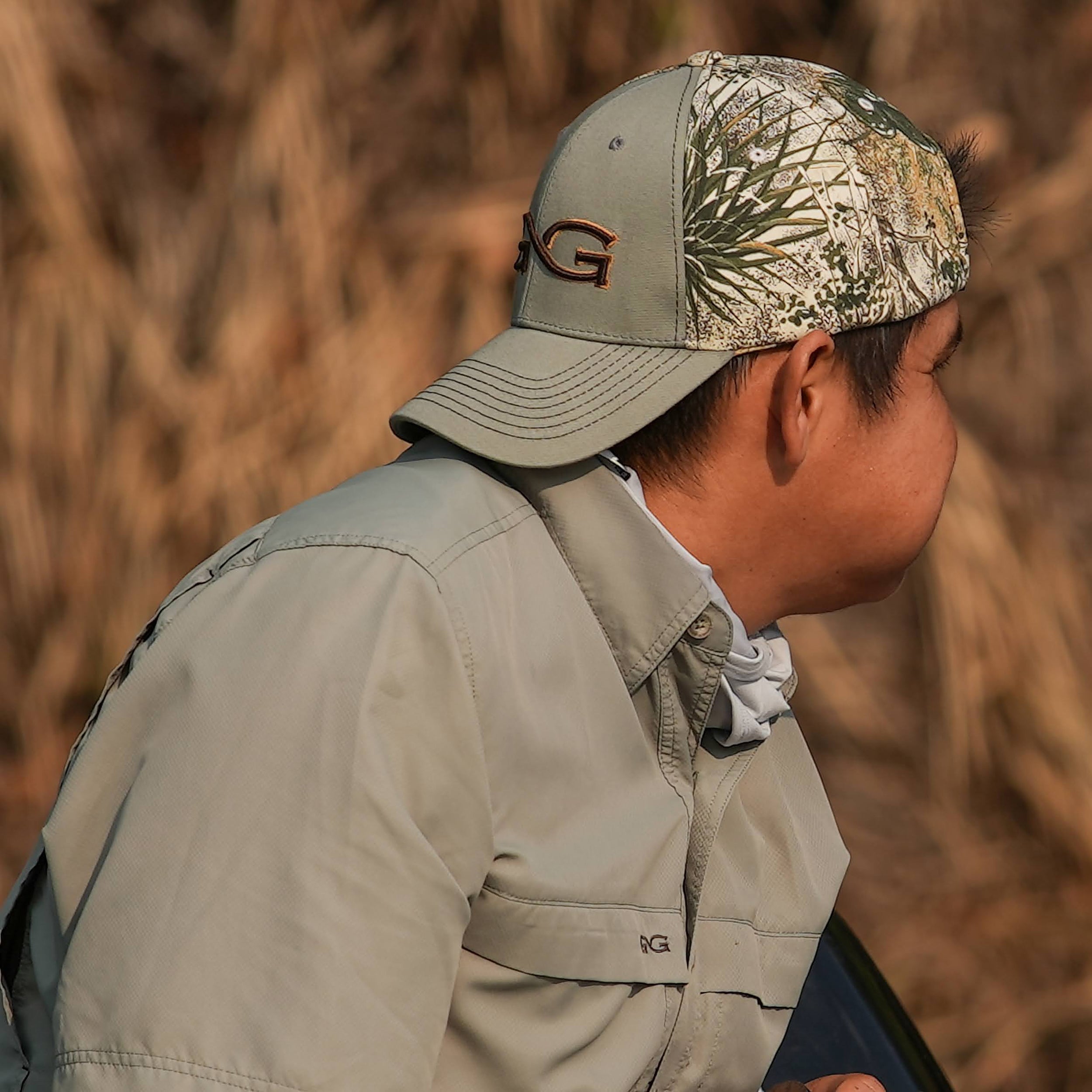 Person wearing a camouflage cap and beige jacket in a natural setting
