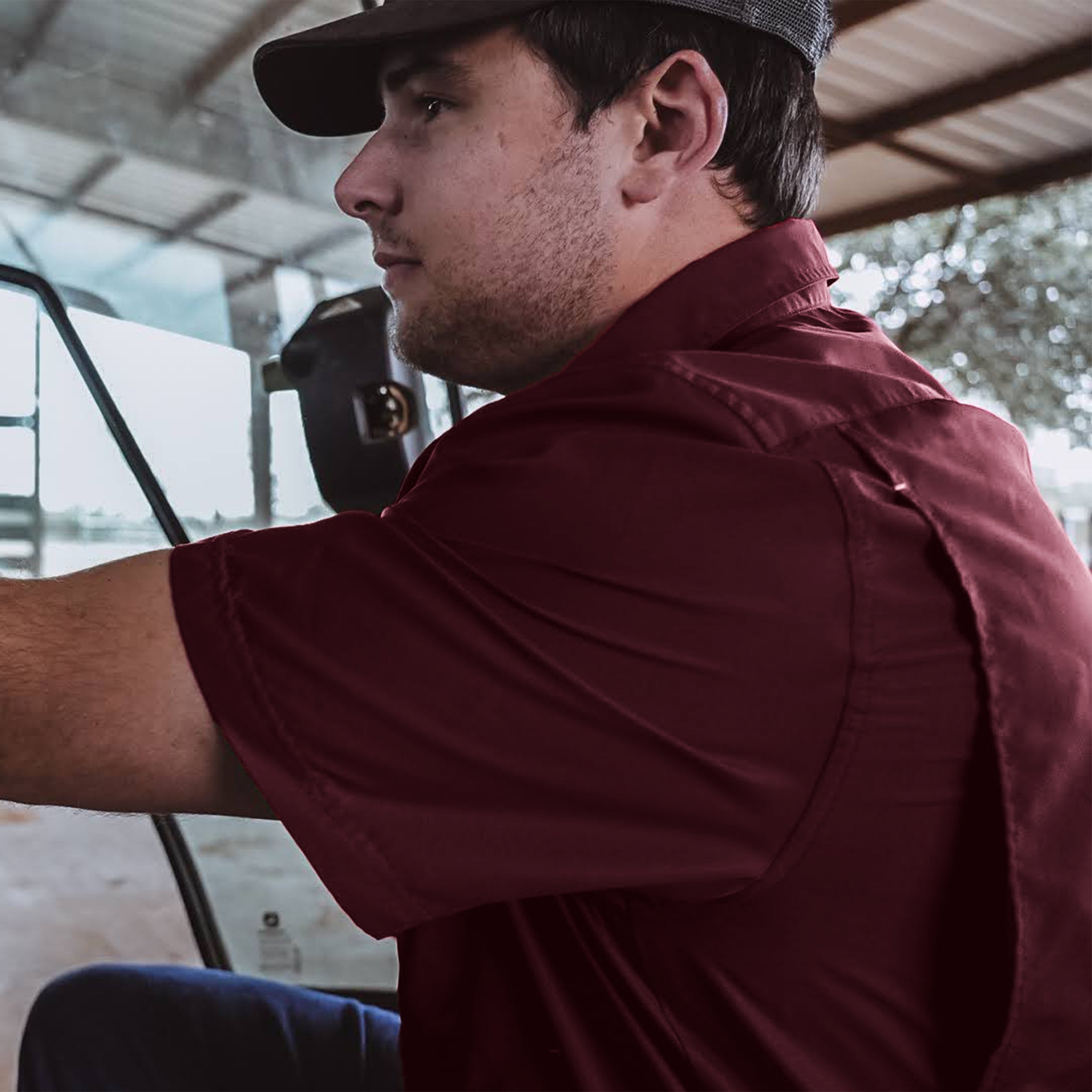Man in a maroon shirt and cap looking out of a vehicle window.