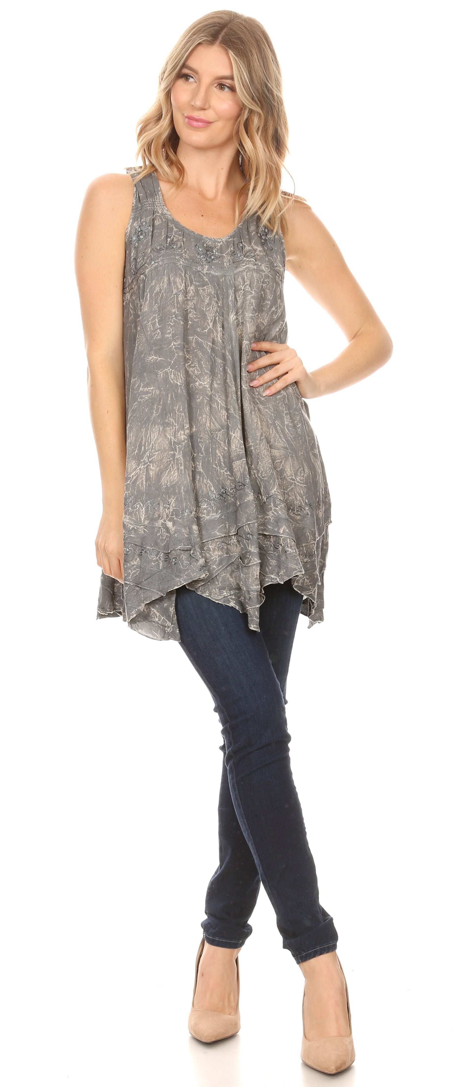 Woman wearing a sleeveless patterned top and dark jeans on a white background