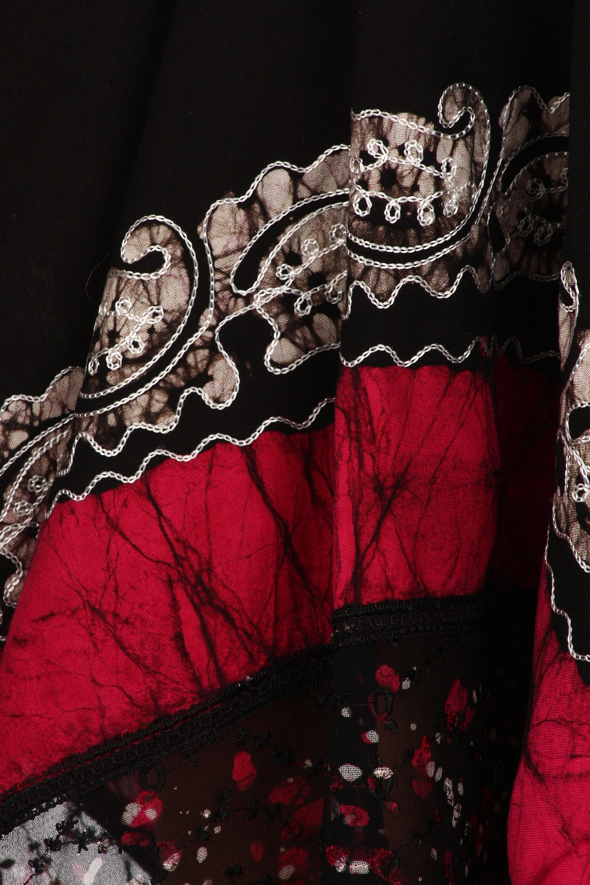Close-up of a red fabric with intricate black and gold embroidery on a dark background