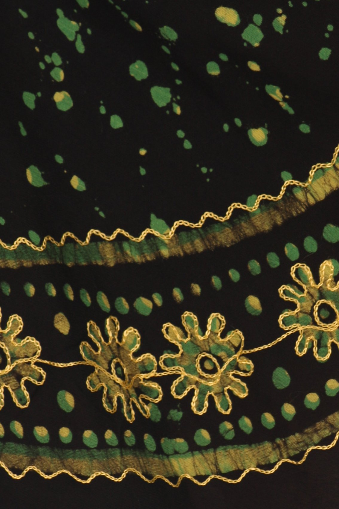 Close-up of a black fabric with green polka dots and gold embroidery.