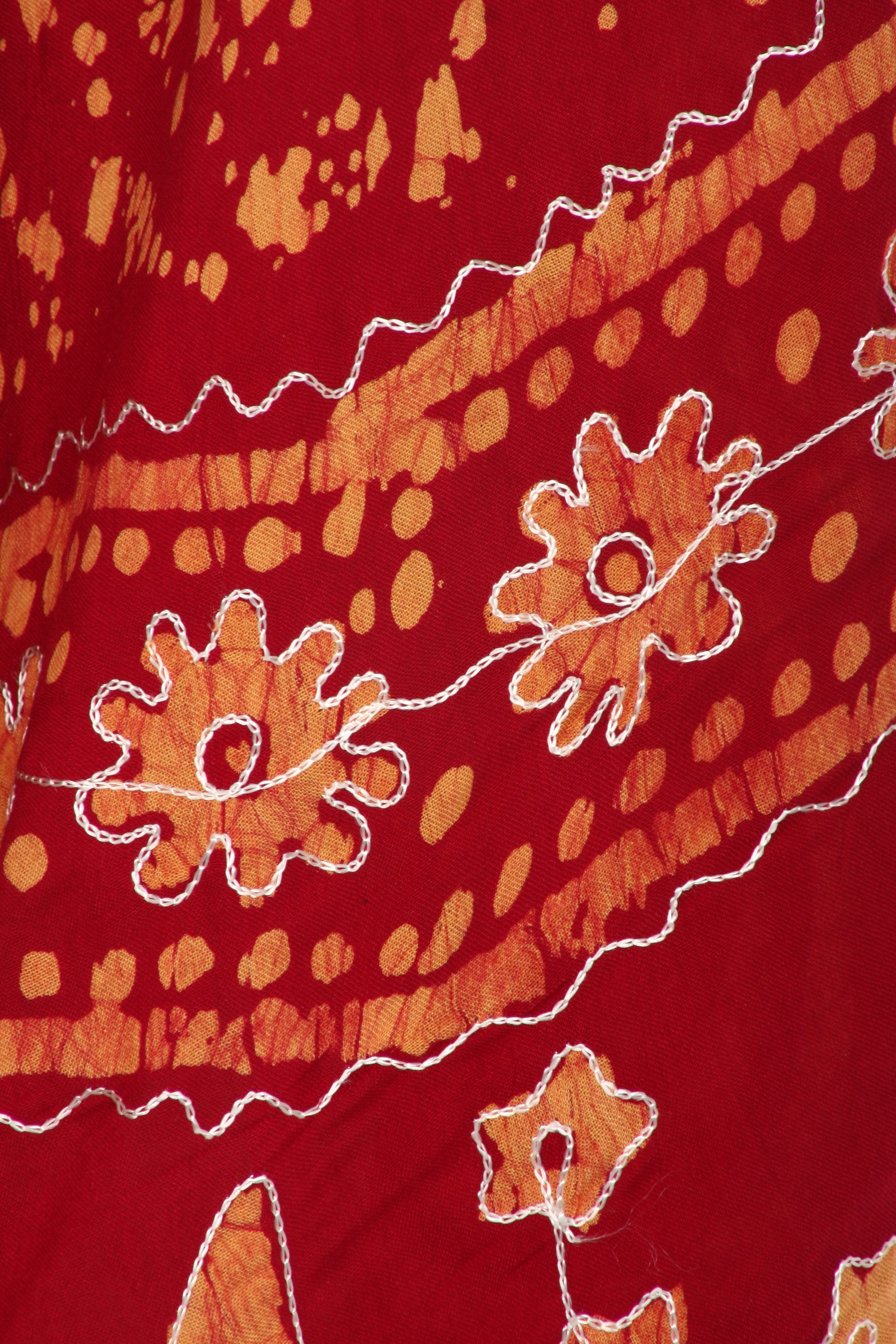 Close-up of a red fabric with orange floral patterns and white stitching.