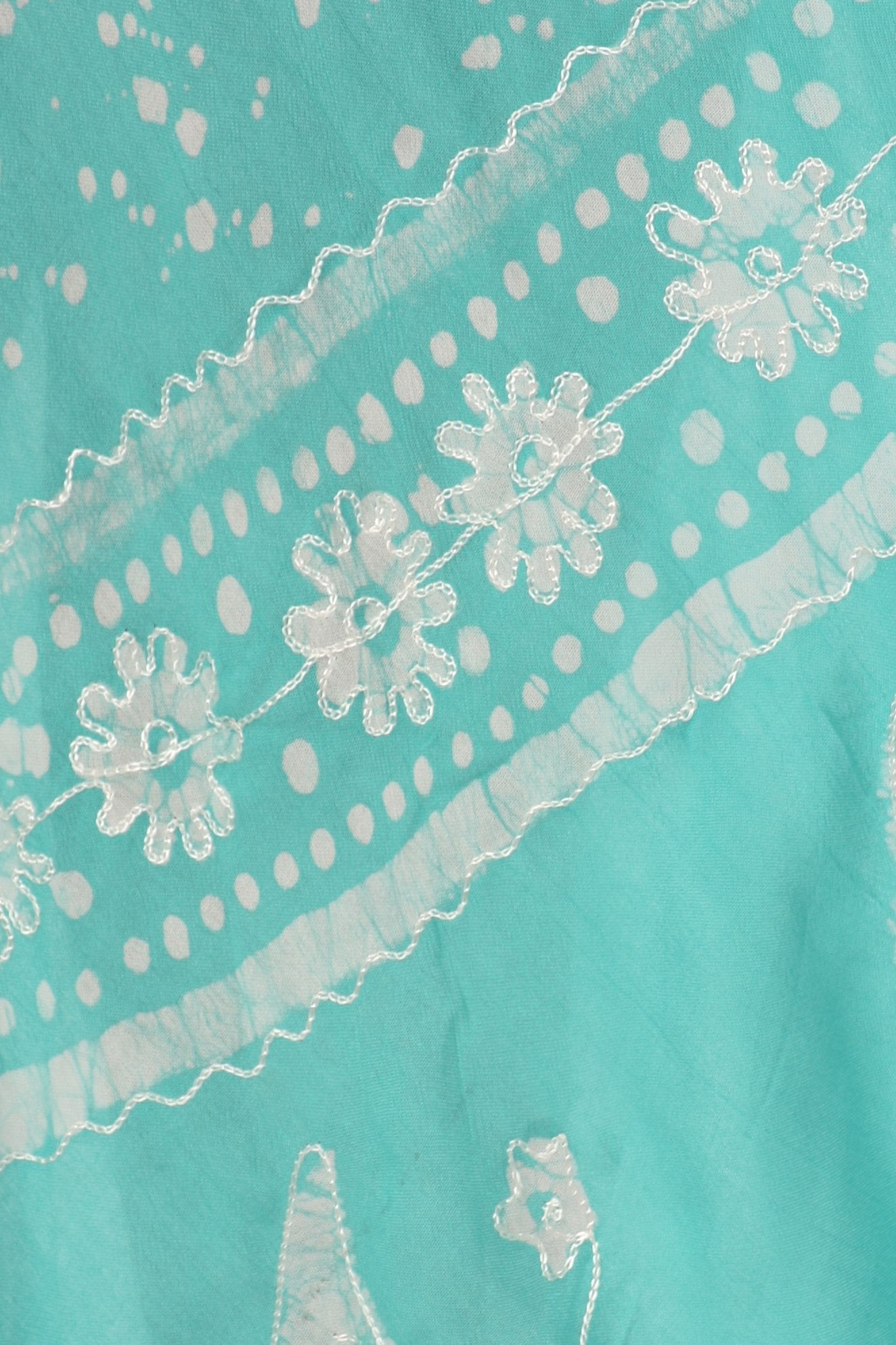 Close-up of turquoise fabric with white lace and floral embroidery