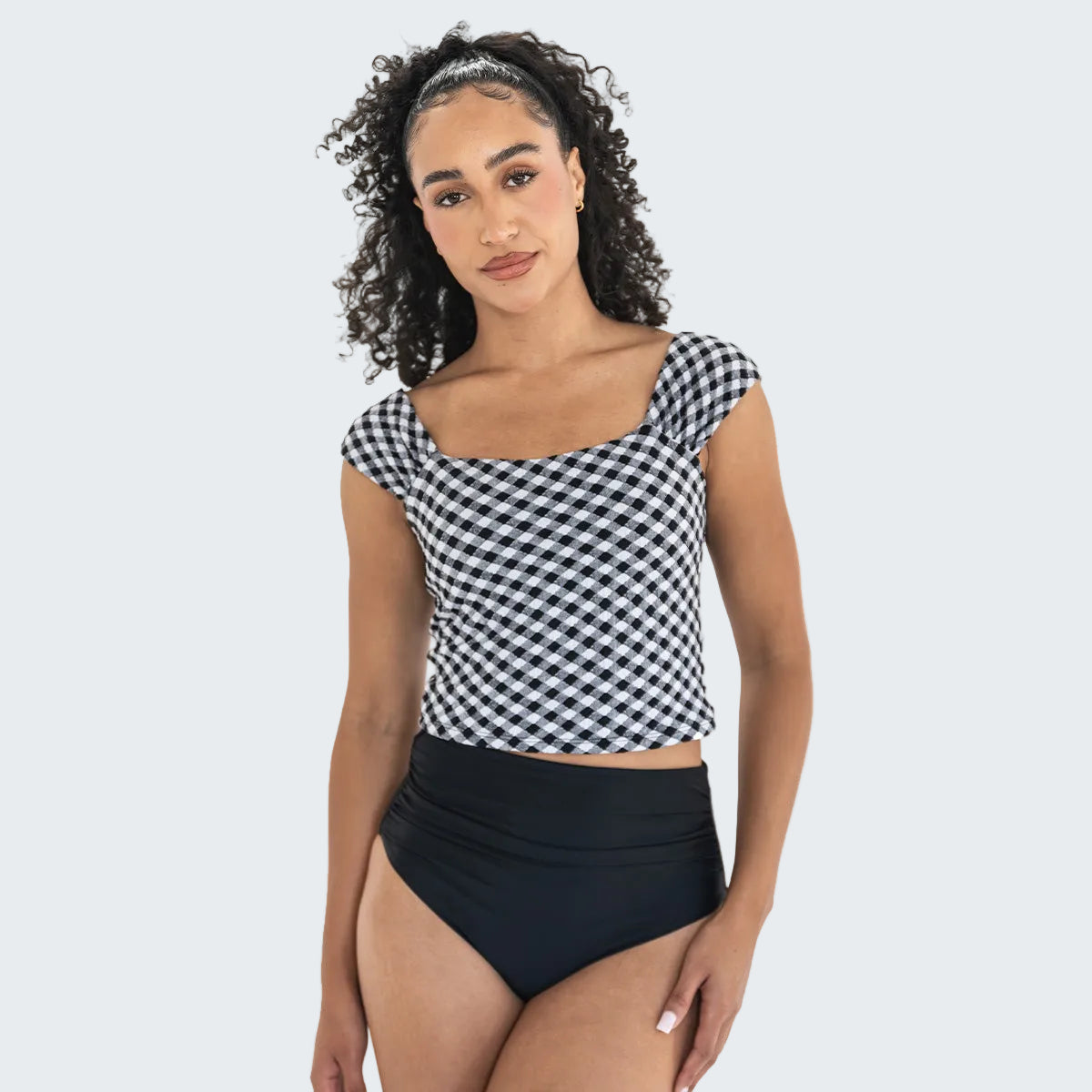 Woman wearing a black and white checkered top and black high-waisted bottoms on a white background