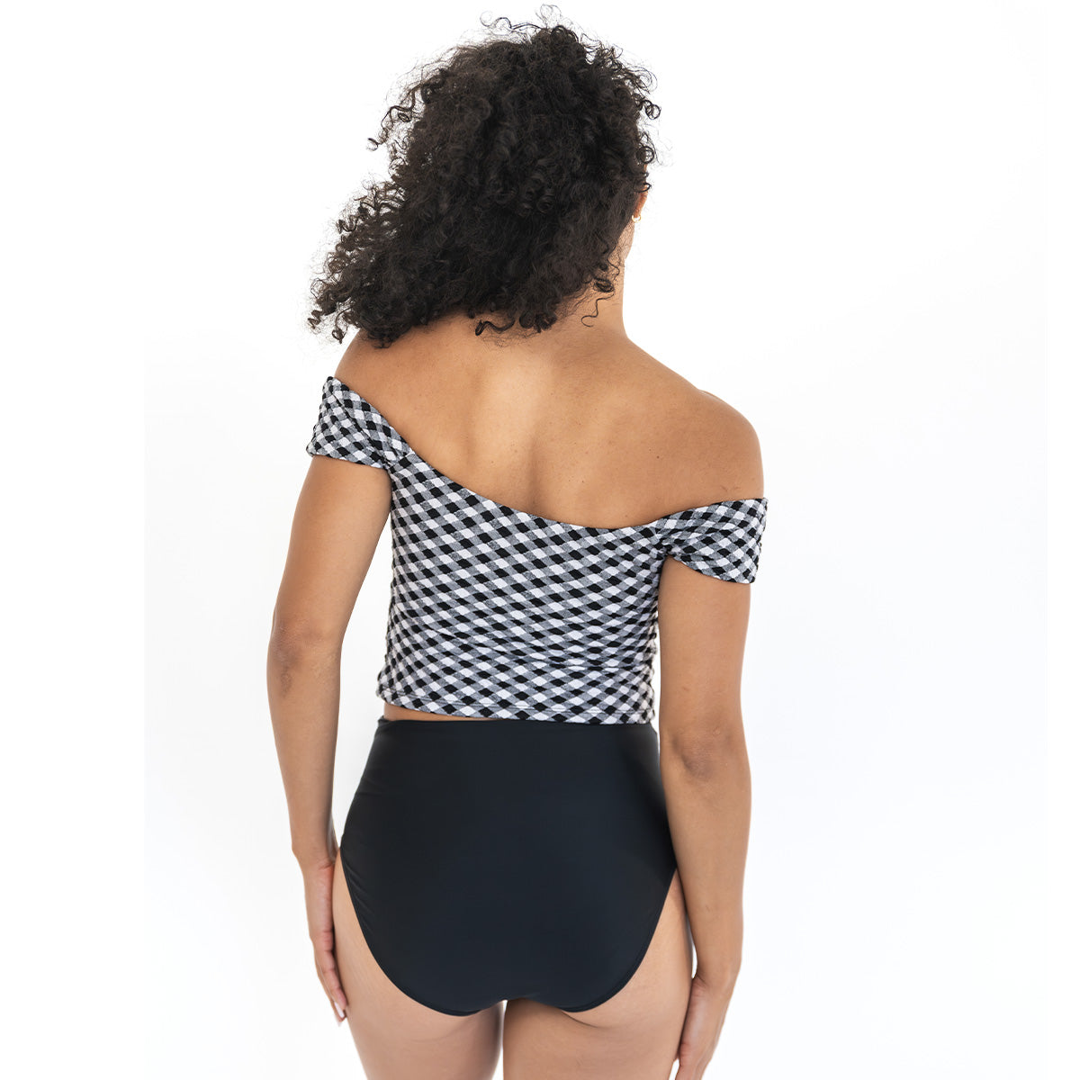 Woman wearing a black and white checkered off-shoulder top with a black high-waisted bottom on a white background