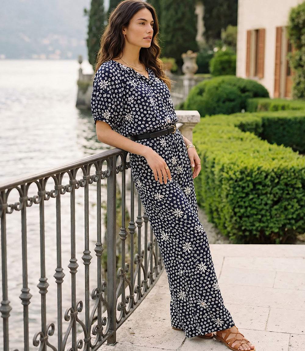 Woman in a floral dress standing by a railing with a scenic background