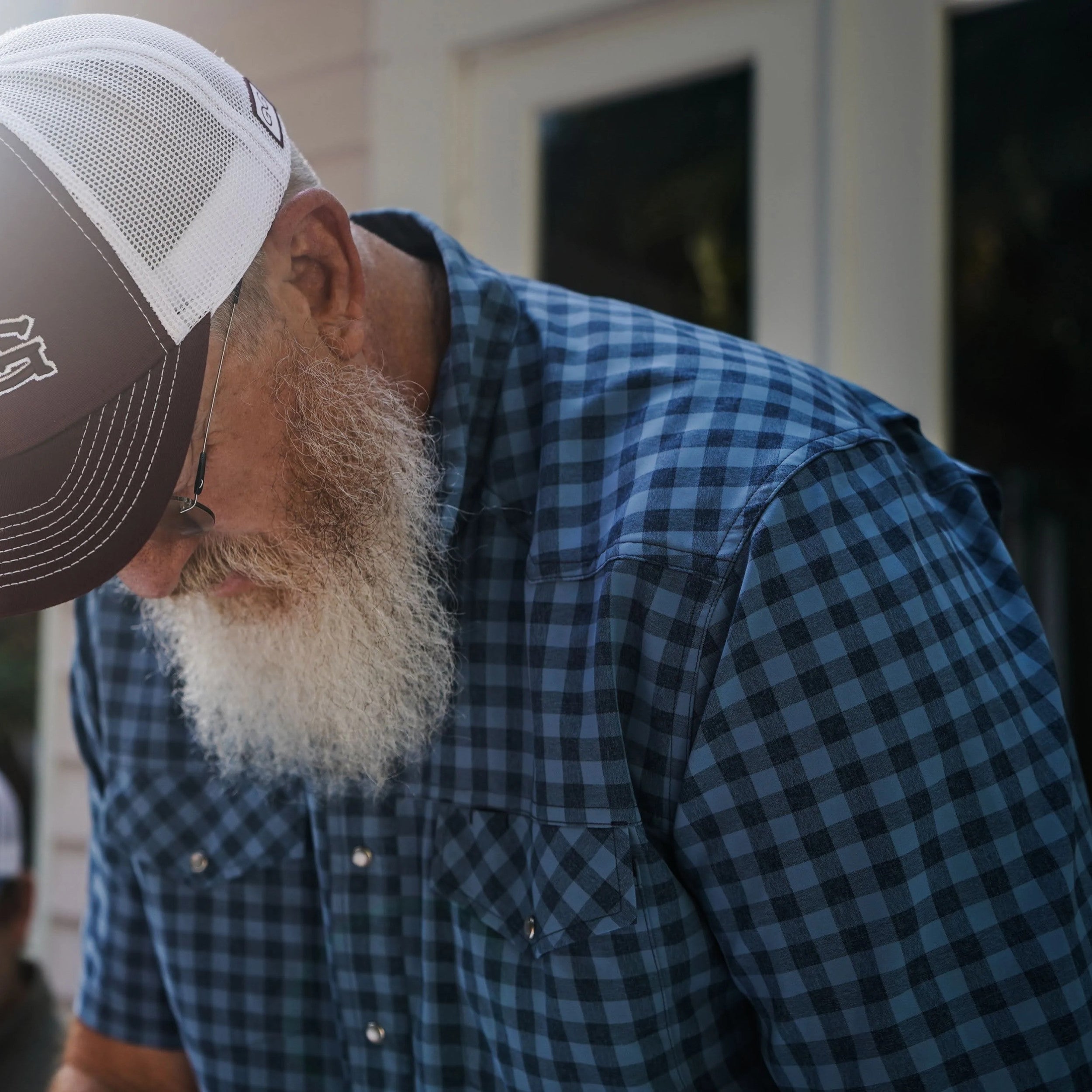 Man wearing a blue plaid shirt and a cap, looking down.