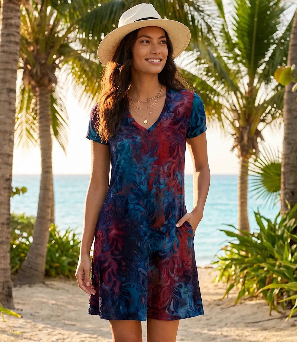 Woman in a colorful dress and hat standing on a beach with palm trees and ocean in the background