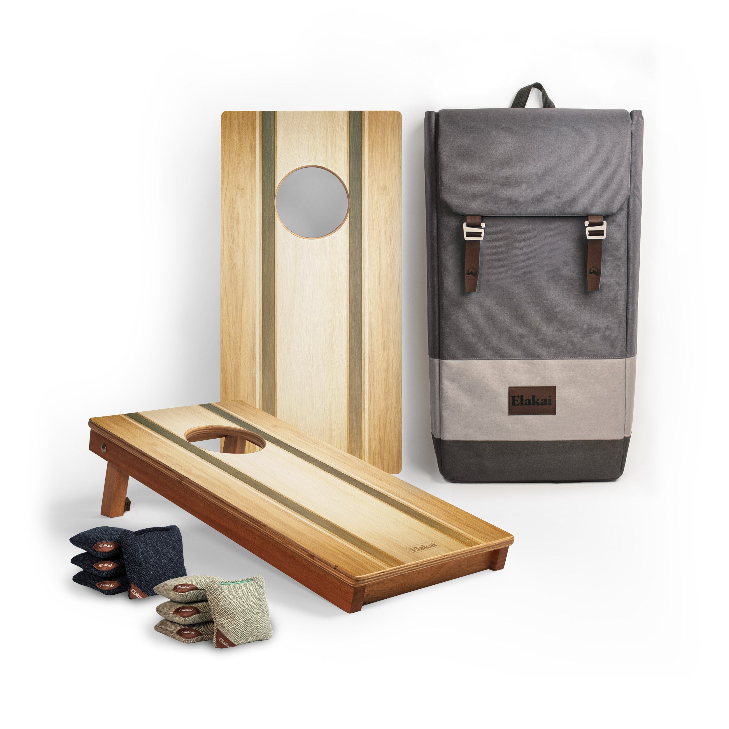 A cornhole set displayed on a white background, including a natural wood cornhole board with a circular hole, a matching wooden board standing upright, a gray fabric backpack with brown leather straps, and several bean bags.