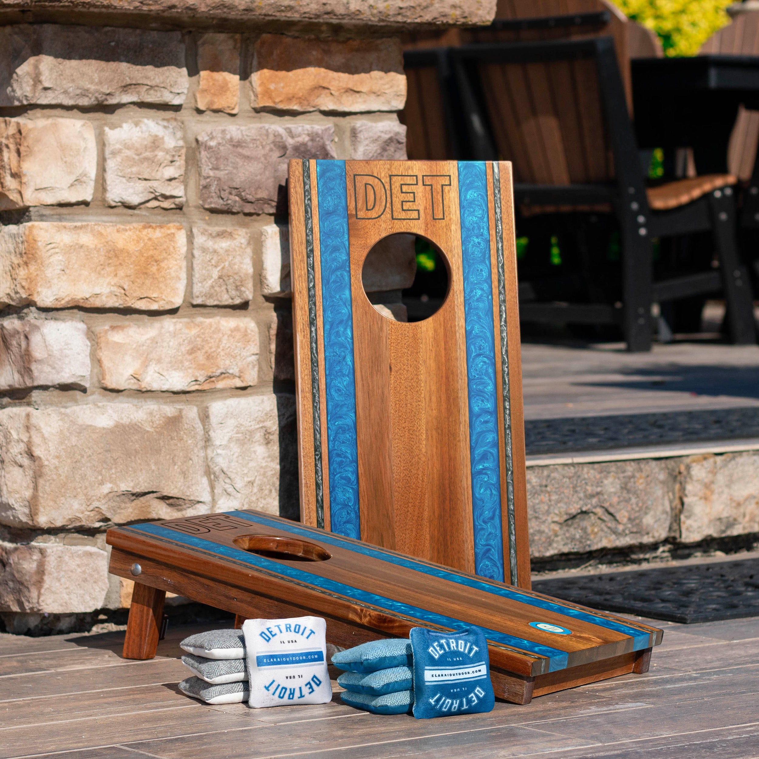 Wooden cornhole board with blue accents and 'DET' branding on a stone patio.