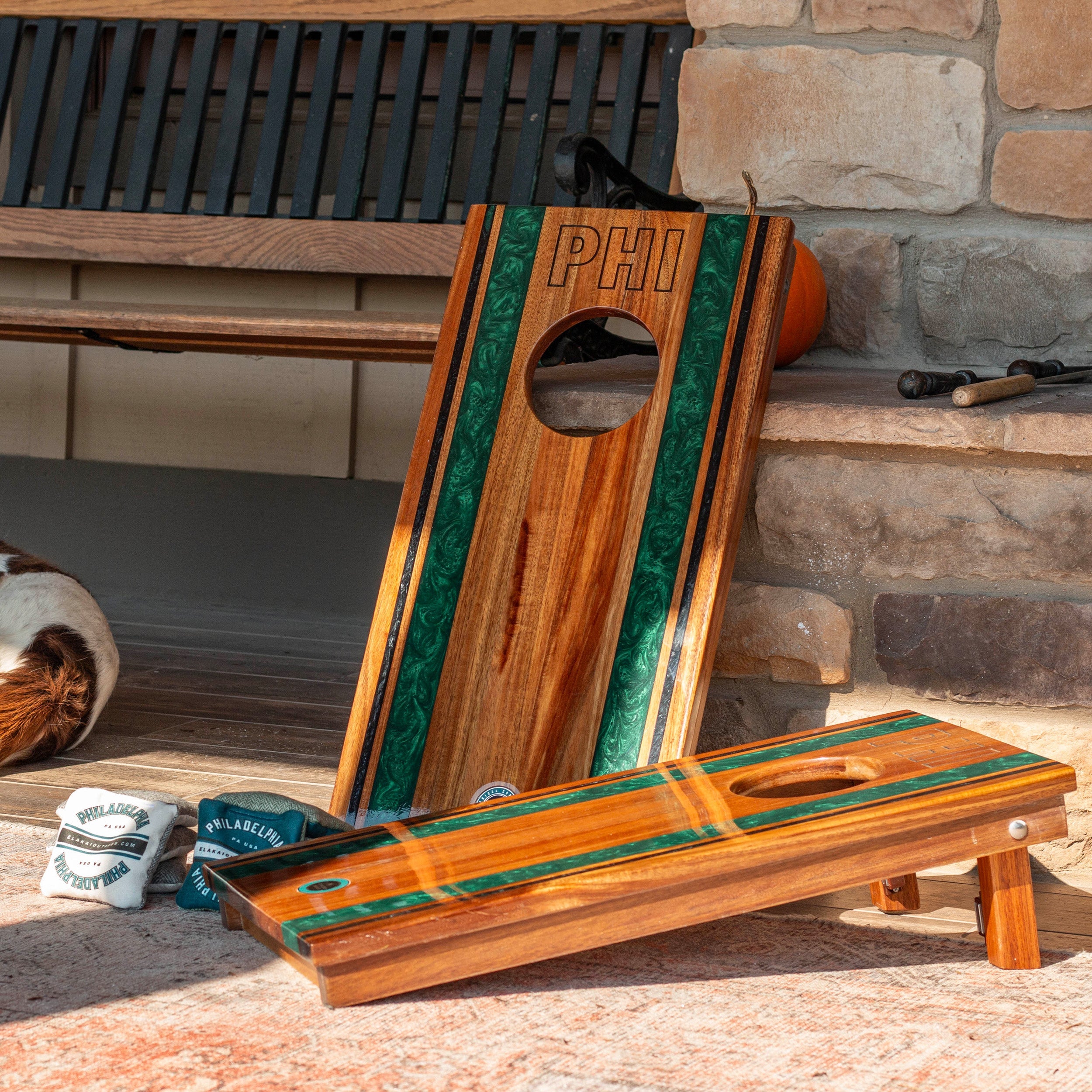 Wooden cornhole boards with green stripe and 'PHI' branding on a stone patio.