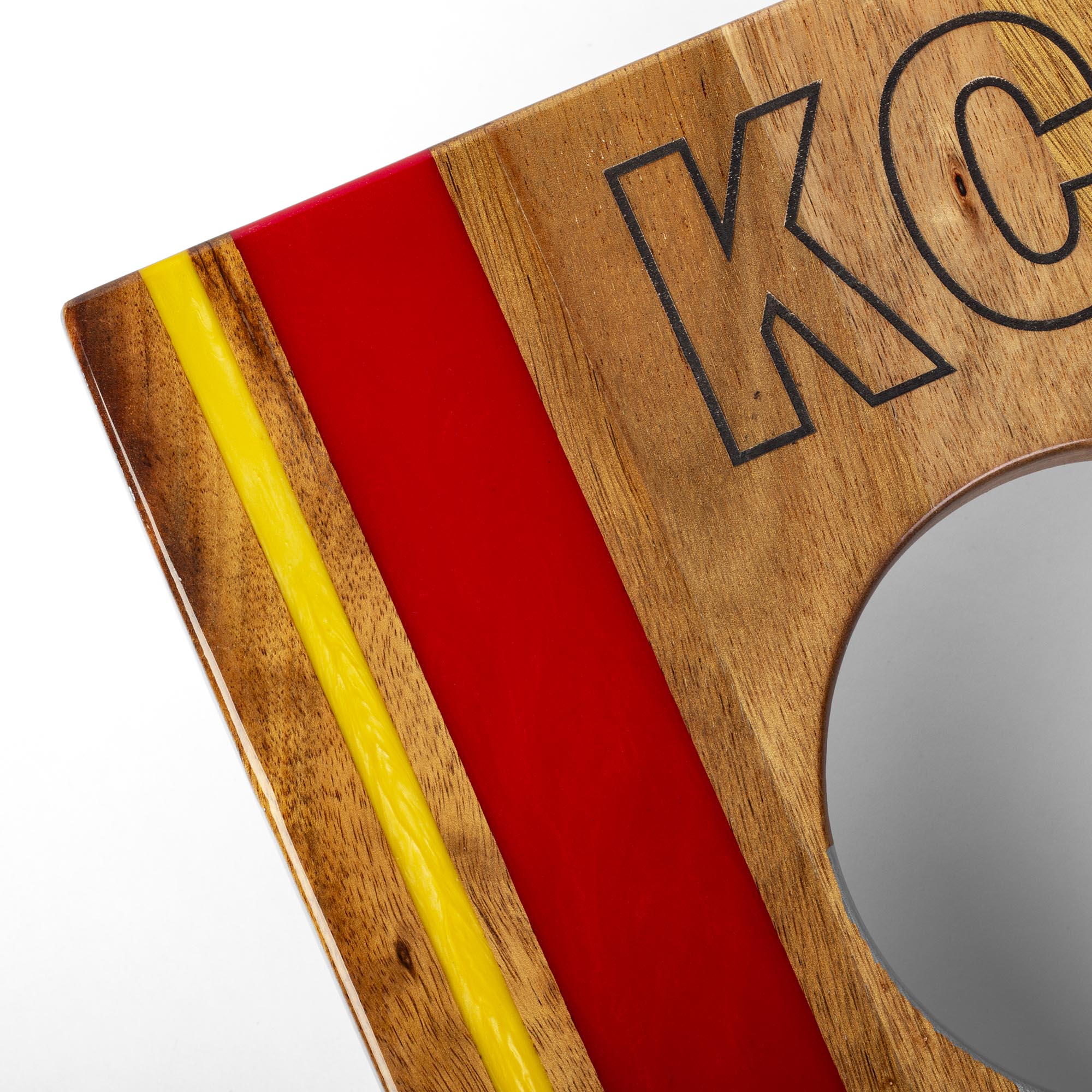 Wooden plaque with 'KC' engraving and red and yellow stripes on a white background