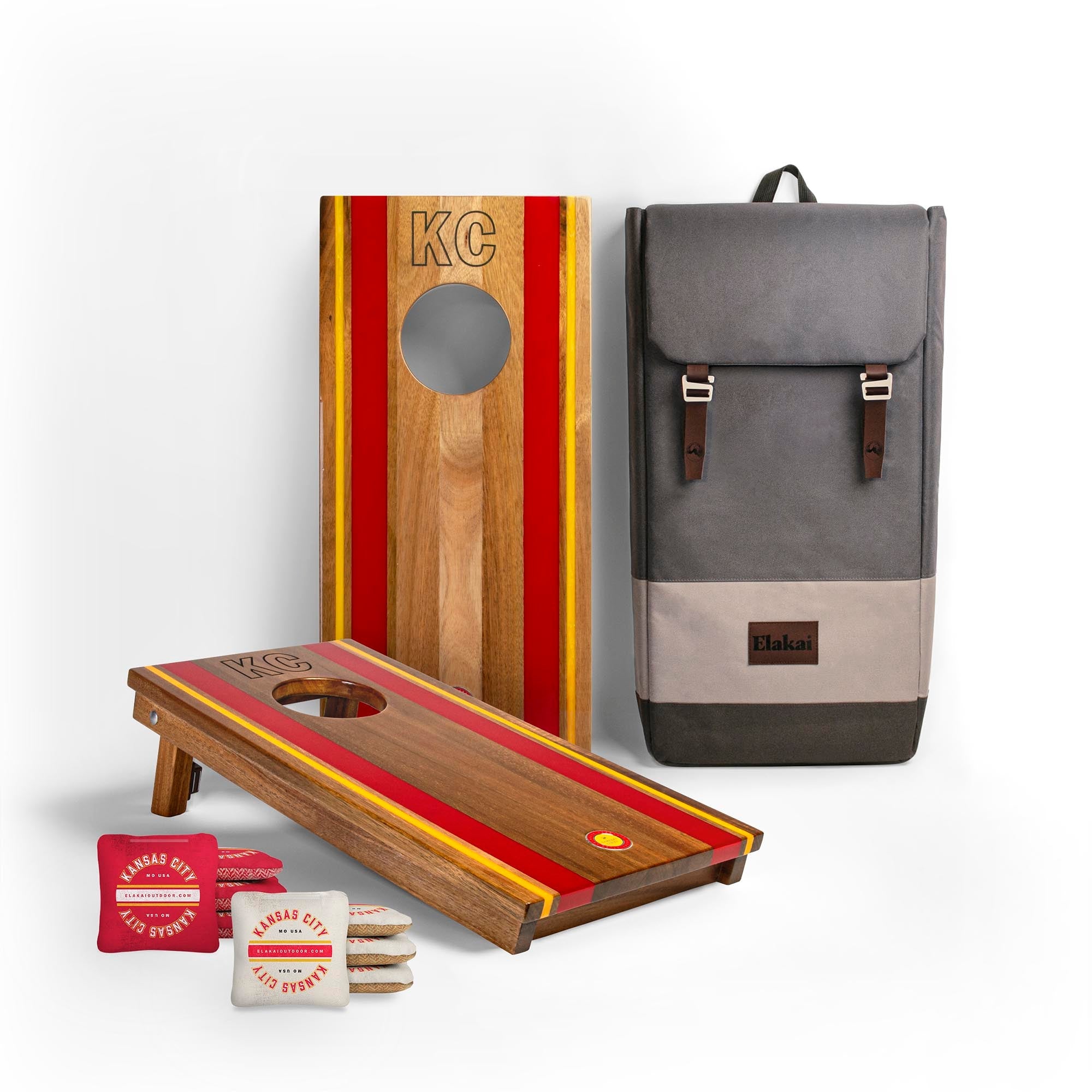 Cornhole boards with red and yellow stripes, a gray backpack, and branded bags on a white background
