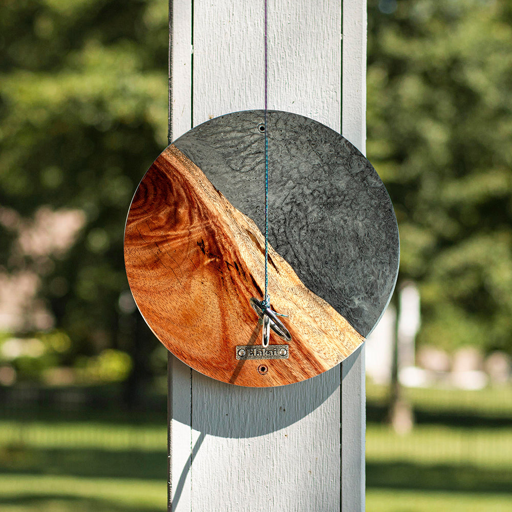 Round wooden and metal wall art piece on a wooden post with a blurred green background