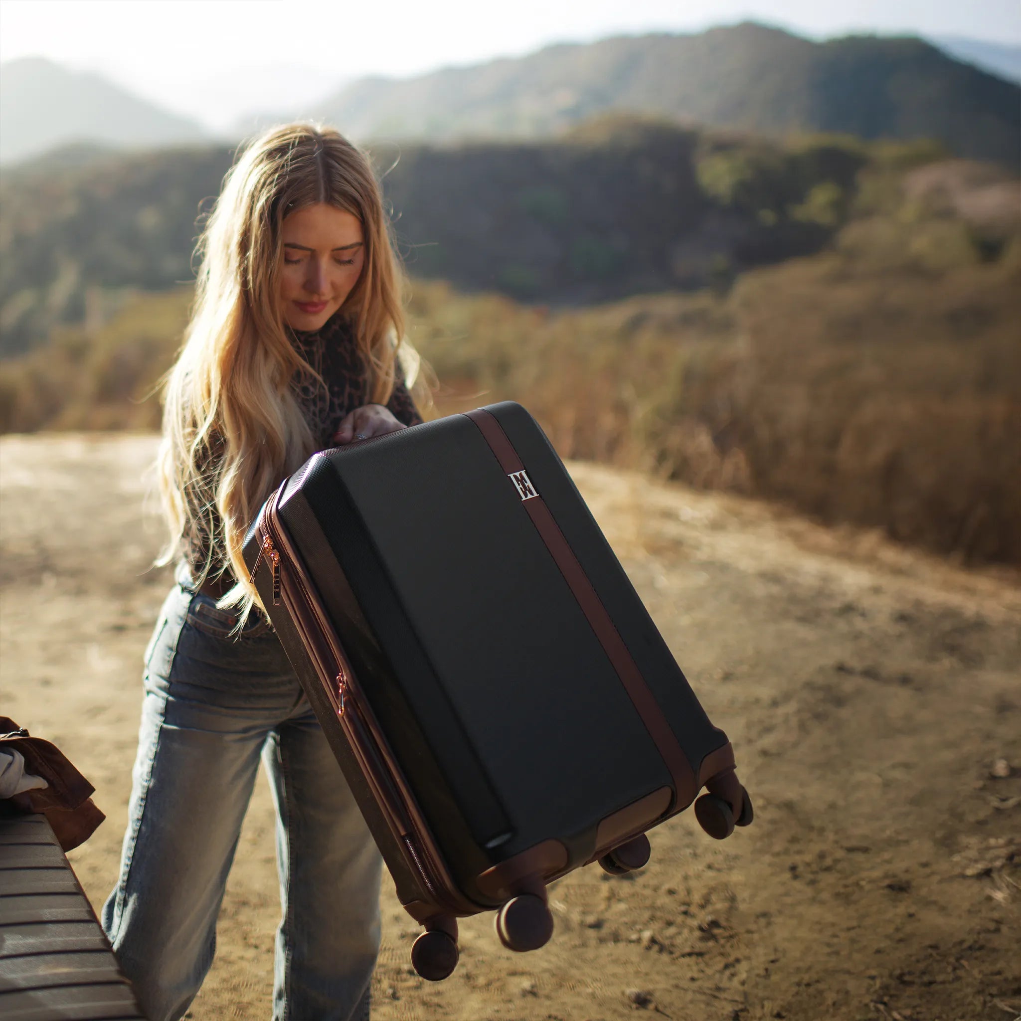 Woman holding a suitcase in a desert landscape with mountains in the background
