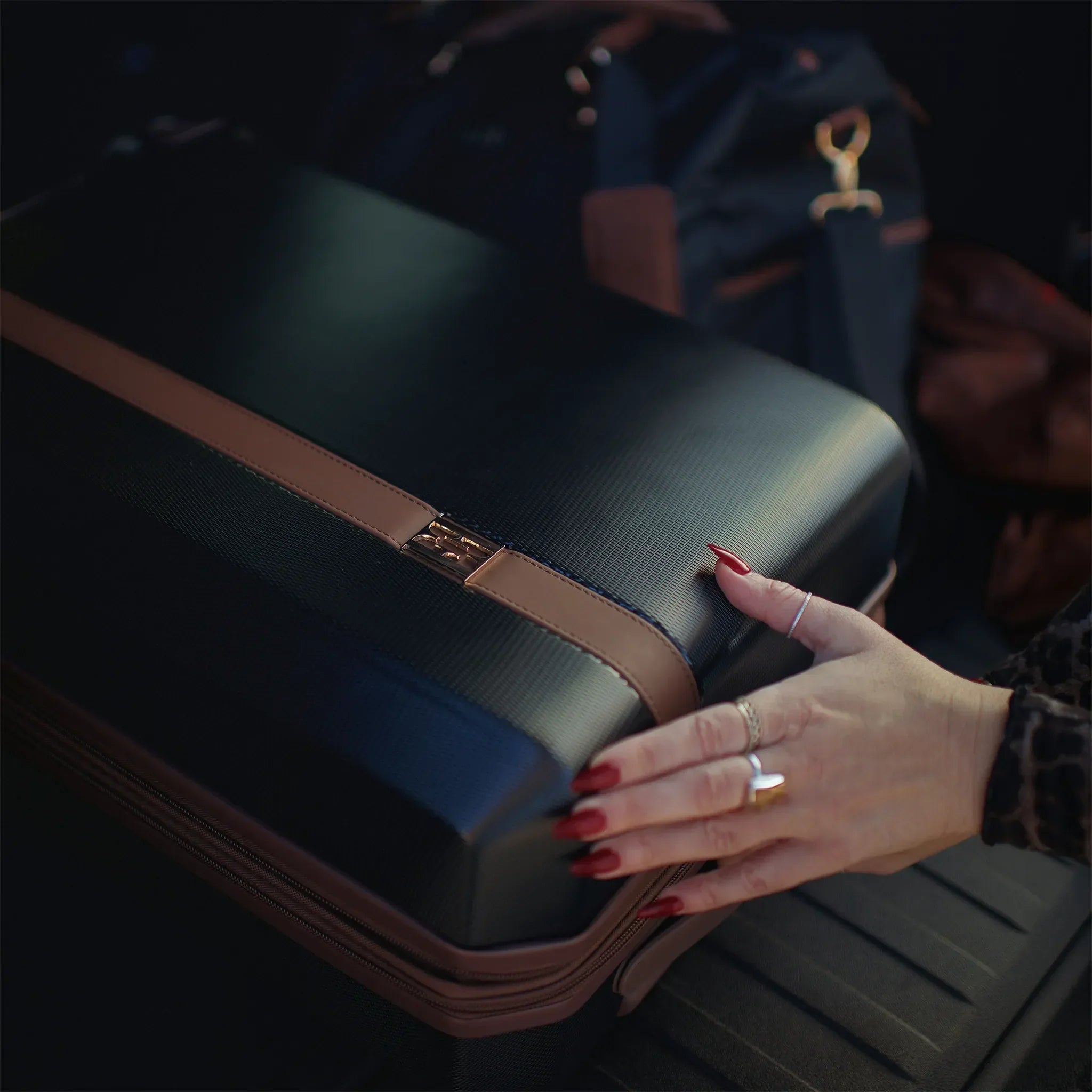 Person holding a suitcase with a handbag in the background