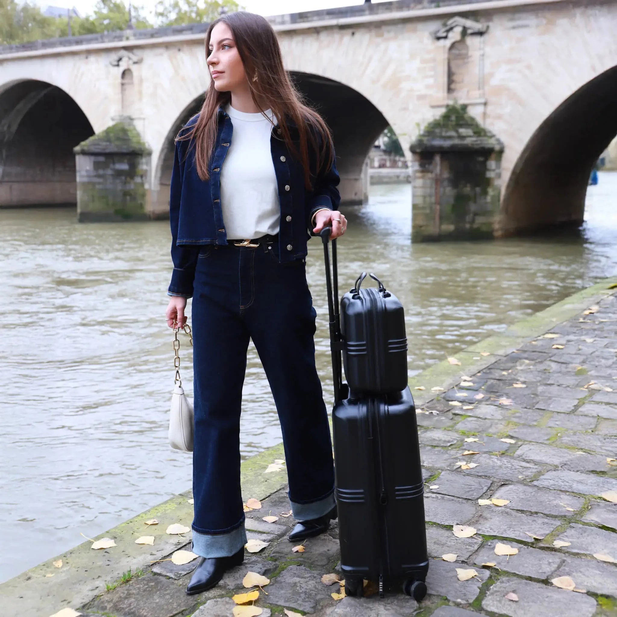 Woman with a suitcase by a river with a bridge in the background