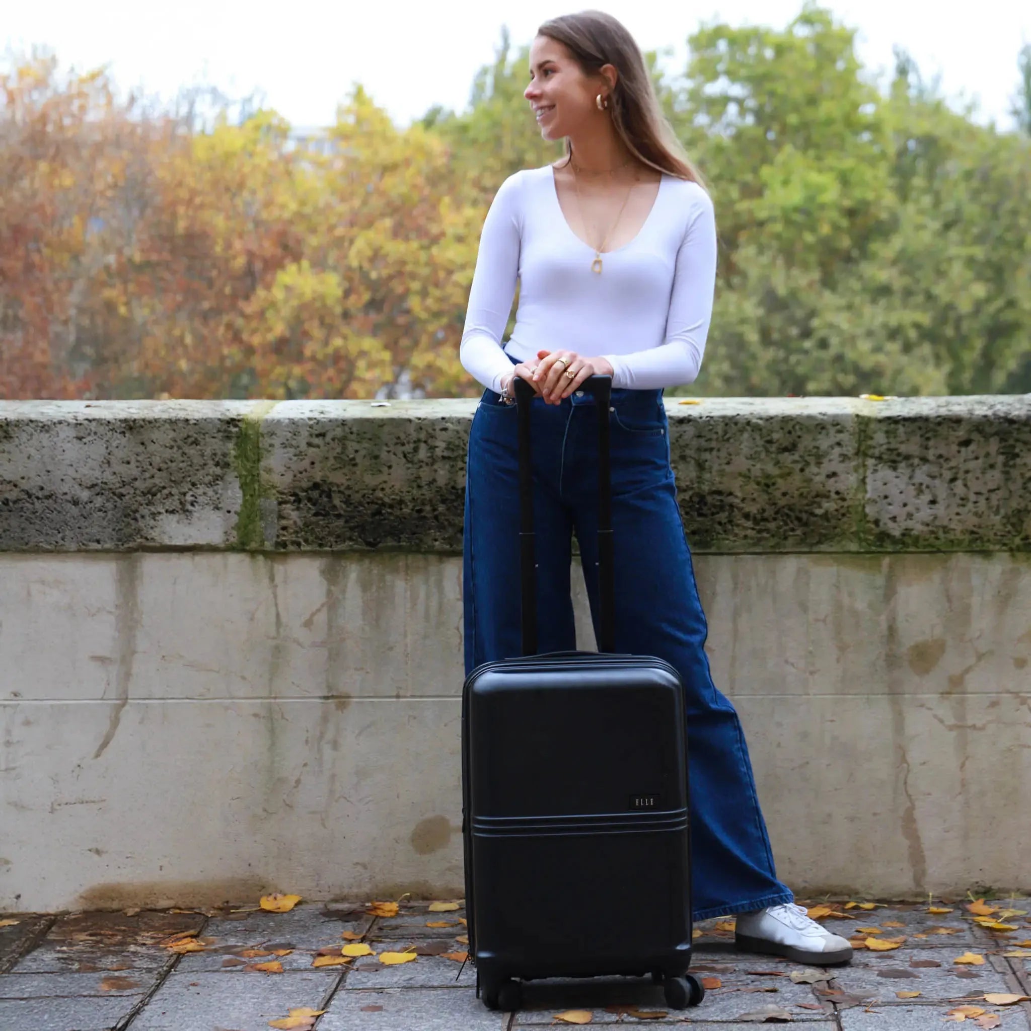 Woman standing next to a black suitcase outdoors with trees in the background