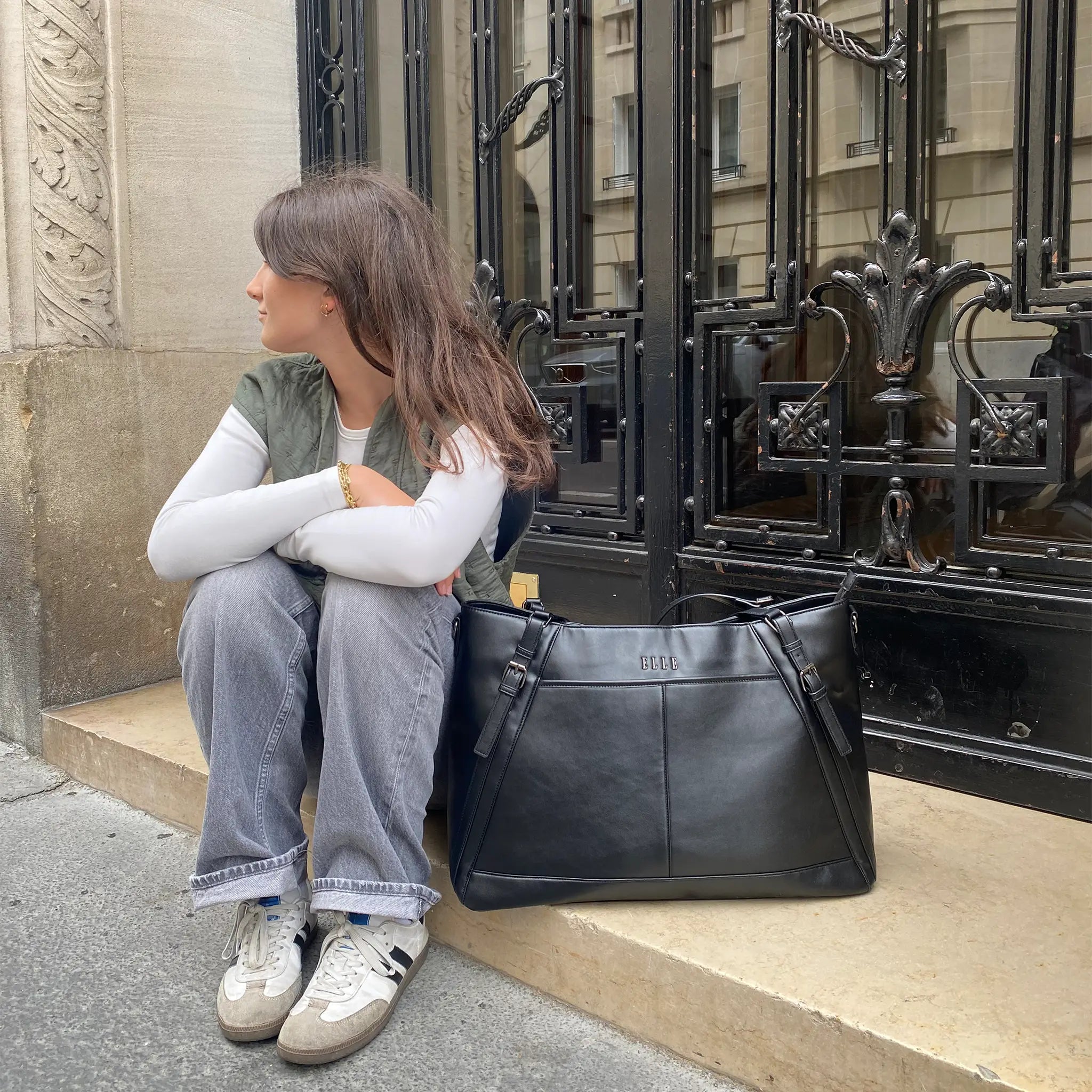 Person sitting on steps with a black leather bag next to them, in front of an ornate metal gate.