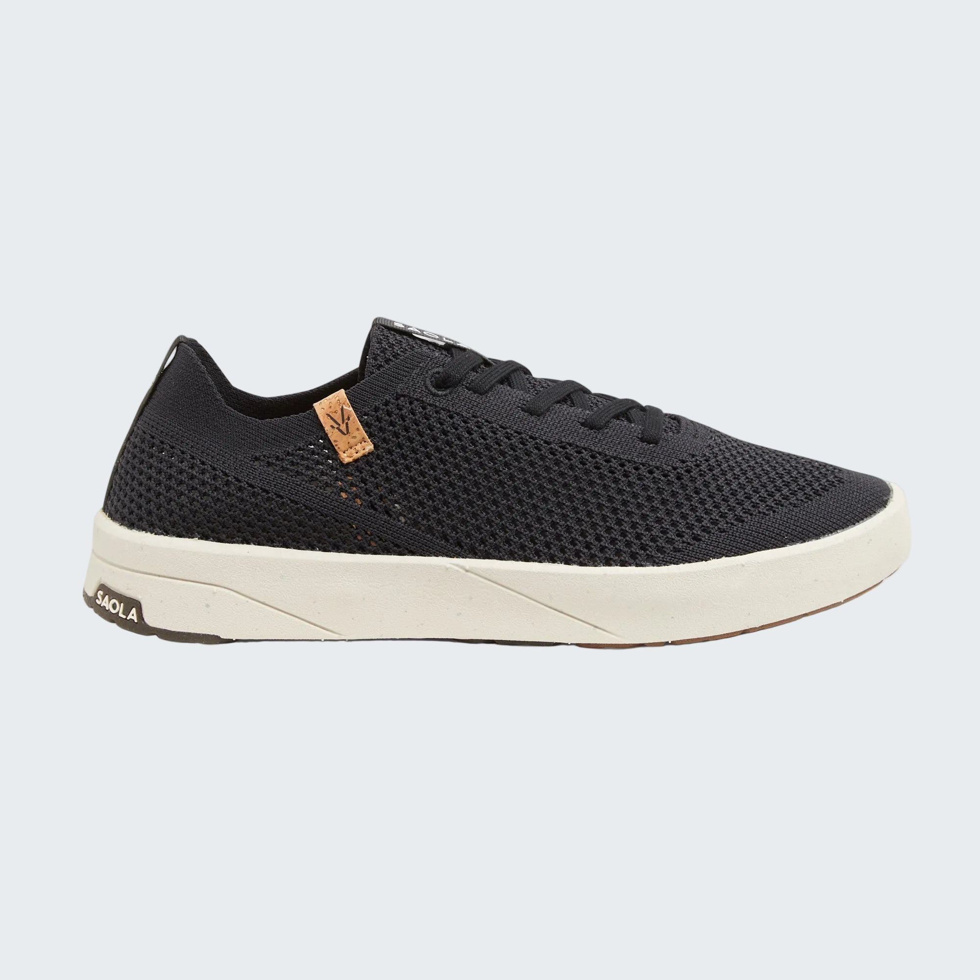 A black mesh low-top sneaker with black laces, a cream-colored midsole, and a small tan brand patch on the side, shown against a light gray background.