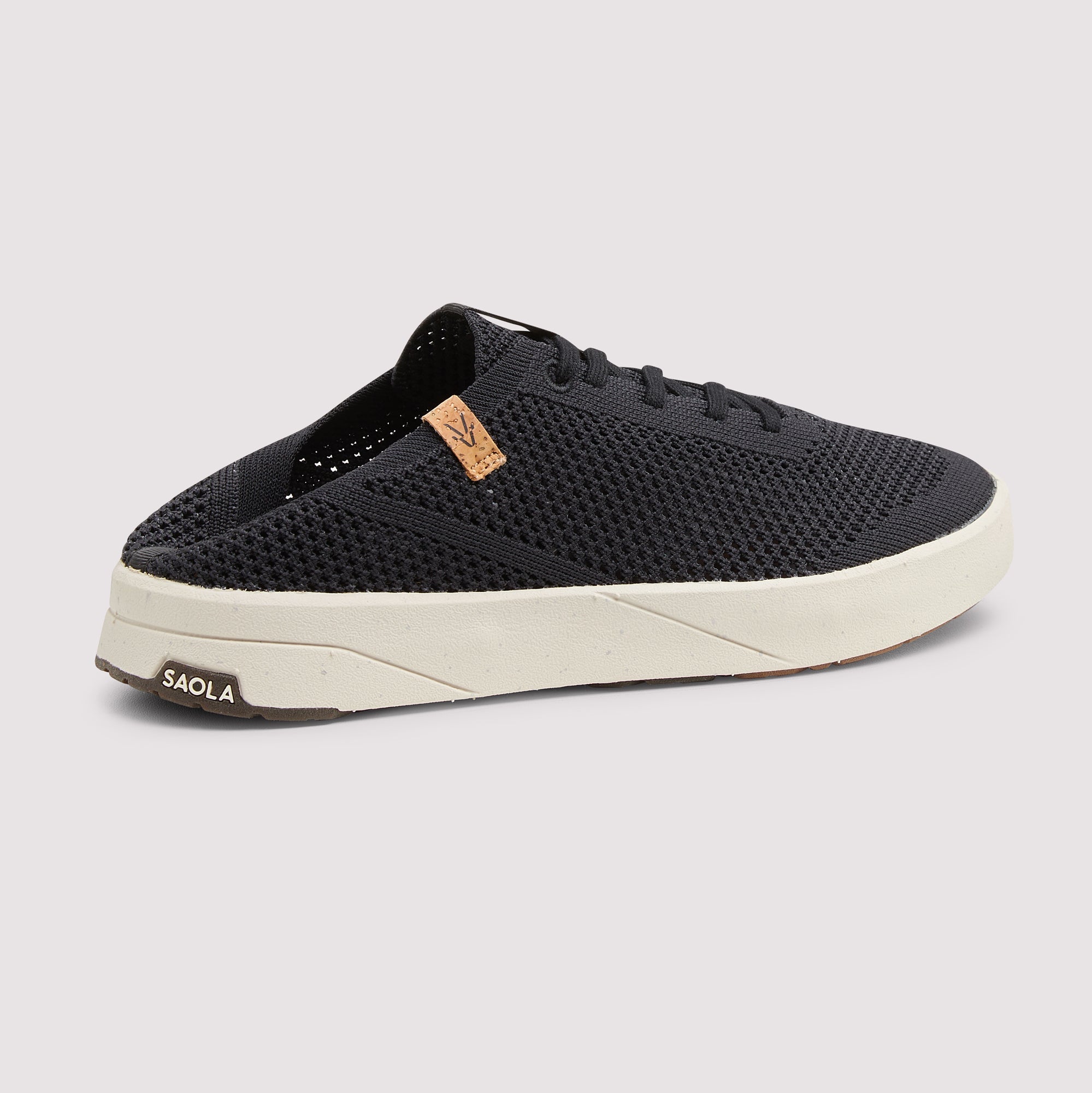 A black mesh slip-on sneaker with a thick off-white sole, featuring a small tan leather logo patch on the side and the brand name 'SAOLA' printed on the heel.