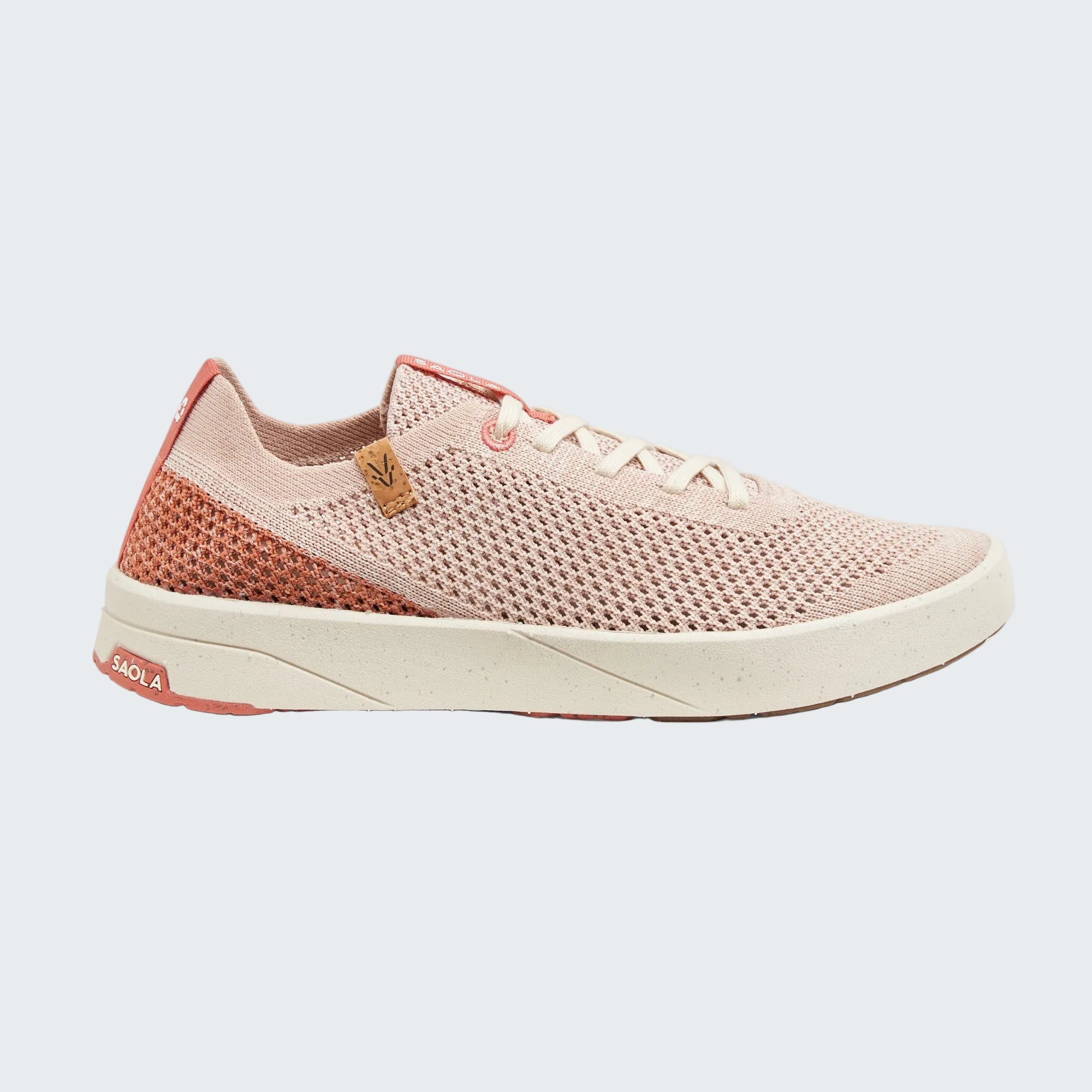 A single low-top athletic sneaker shown in profile against a light gray background. The shoe features a light pink knit upper, a textured coral-pink mesh heel panel, white laces, and a thick white midsole with a small pink 'SOLA' logo on the heel.