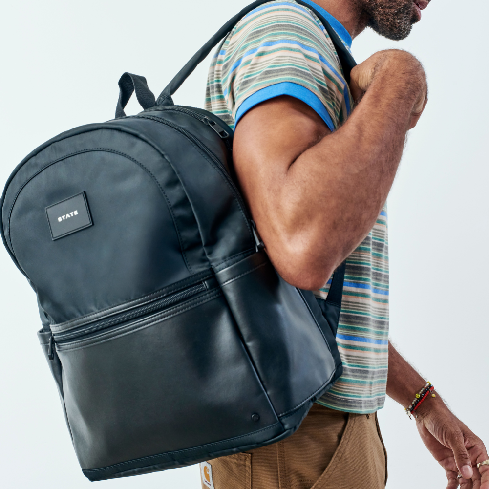Man wearing a black backpack with a visible brand logo on a light gray background