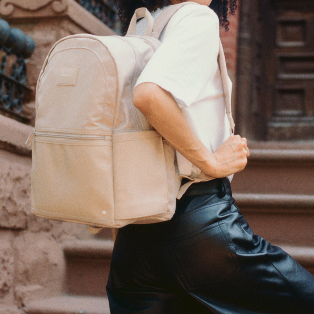 Person wearing a beige backpack walking outdoors.