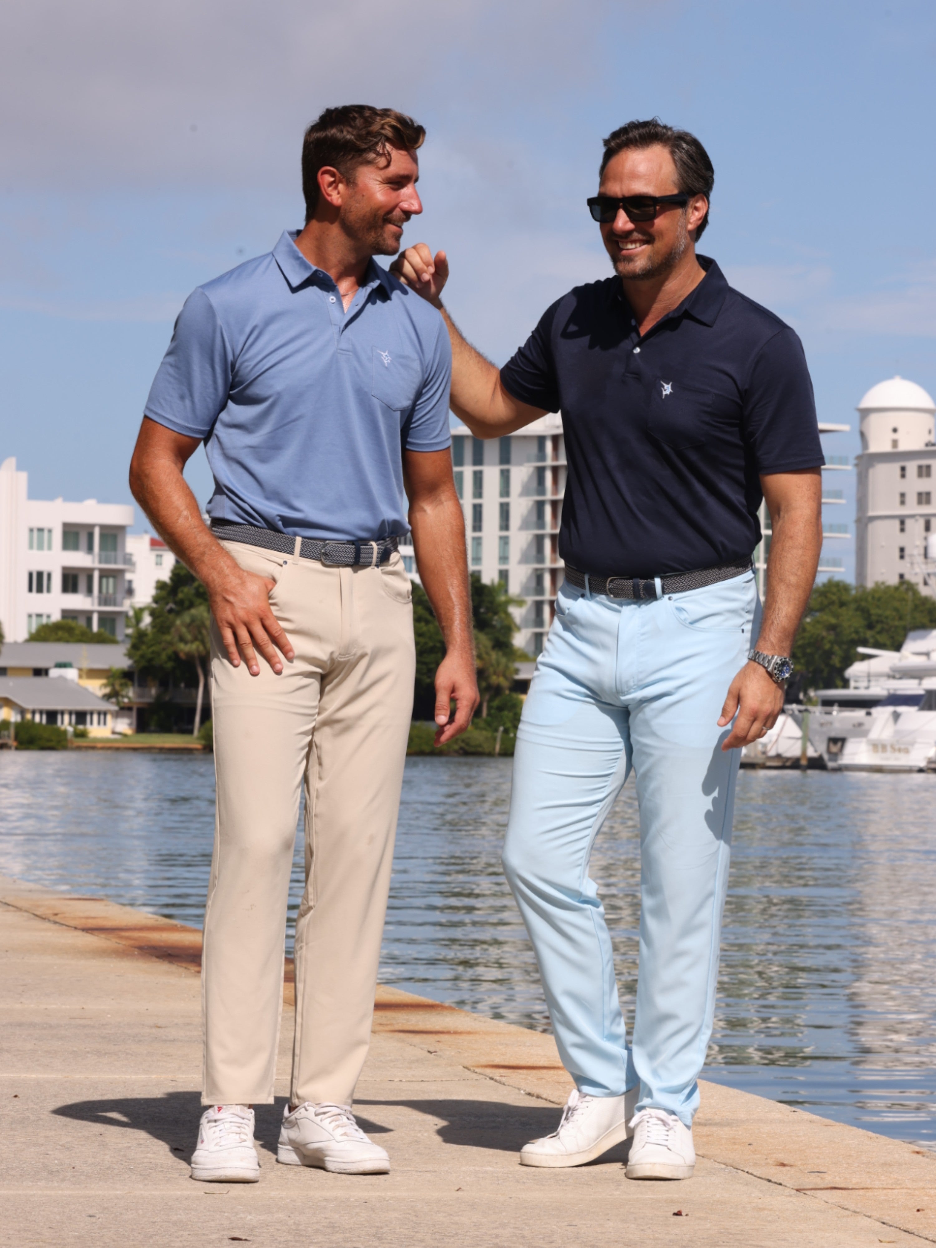 Two men standing on a dock by a waterfront, wearing matching polo shirts and light pants.