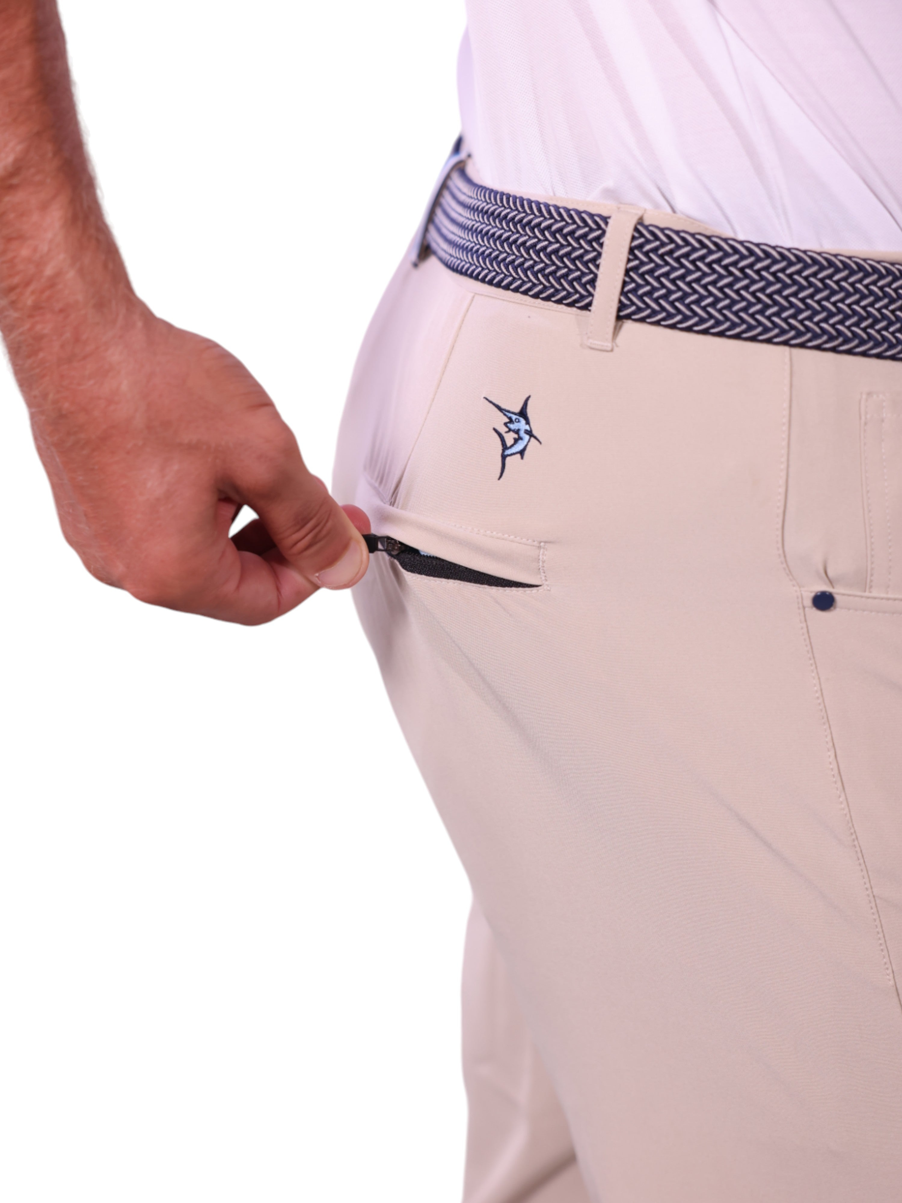 Beige pants with a fish emblem and a person adjusting the waistband on a white background