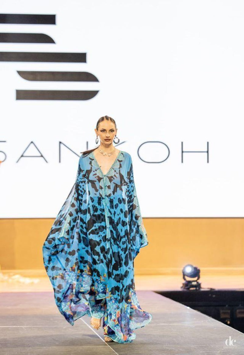Model wearing a blue floral dress on a runway with 'Sankoh' branding.