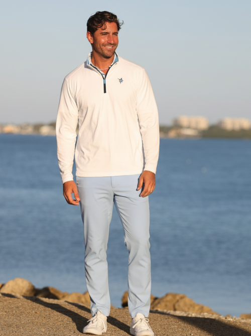 Man standing by a body of water wearing a light-colored jacket and pants.