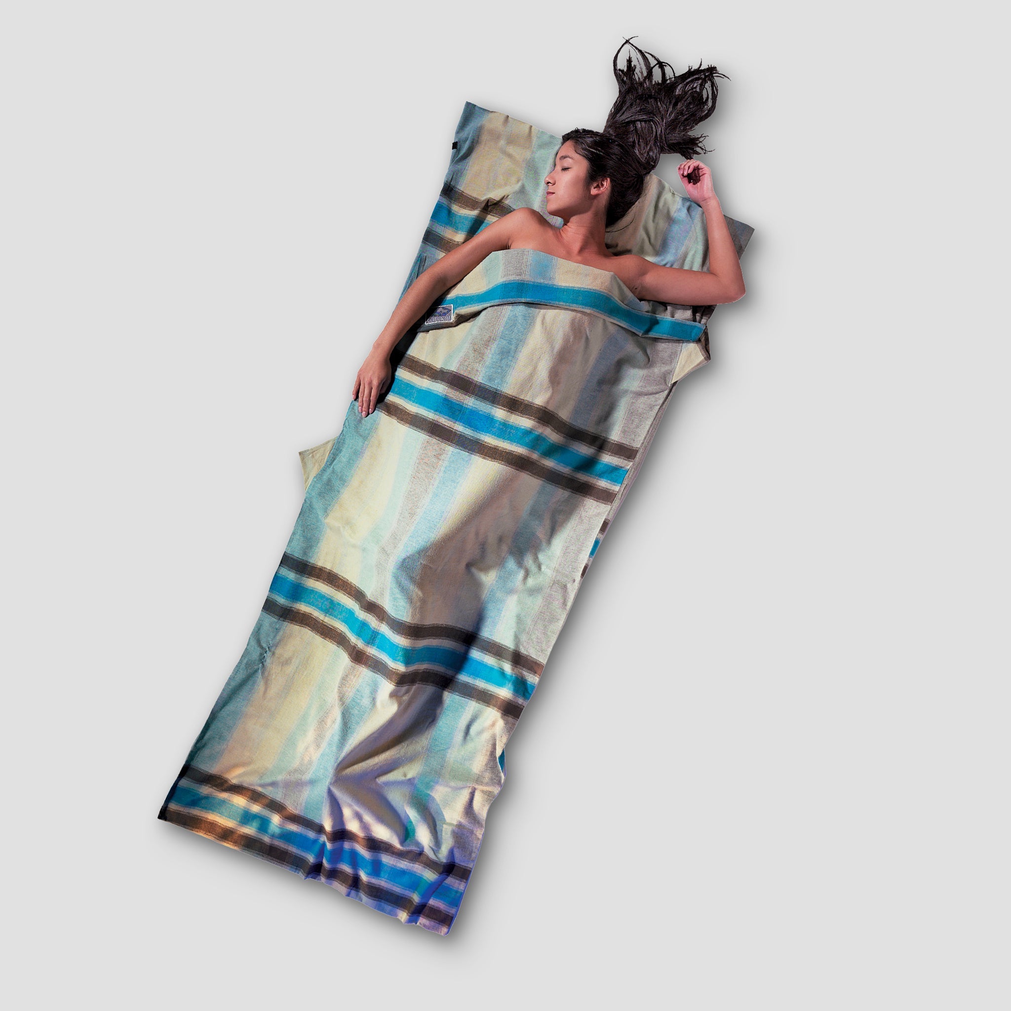 Woman lying on a colorful striped blanket against a plain background