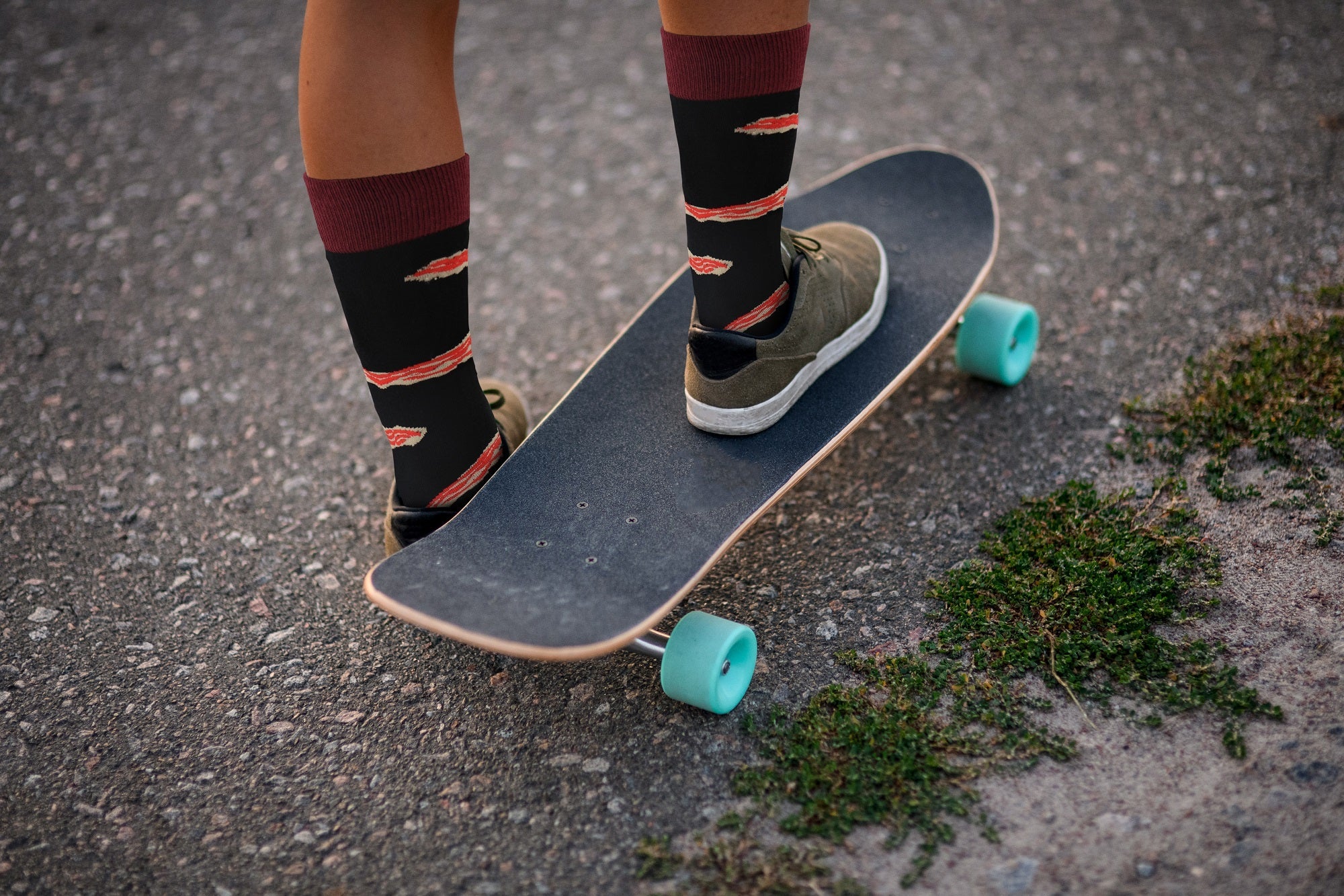Person standing on a skateboard with colorful socks and shoes on an asphalt surface.