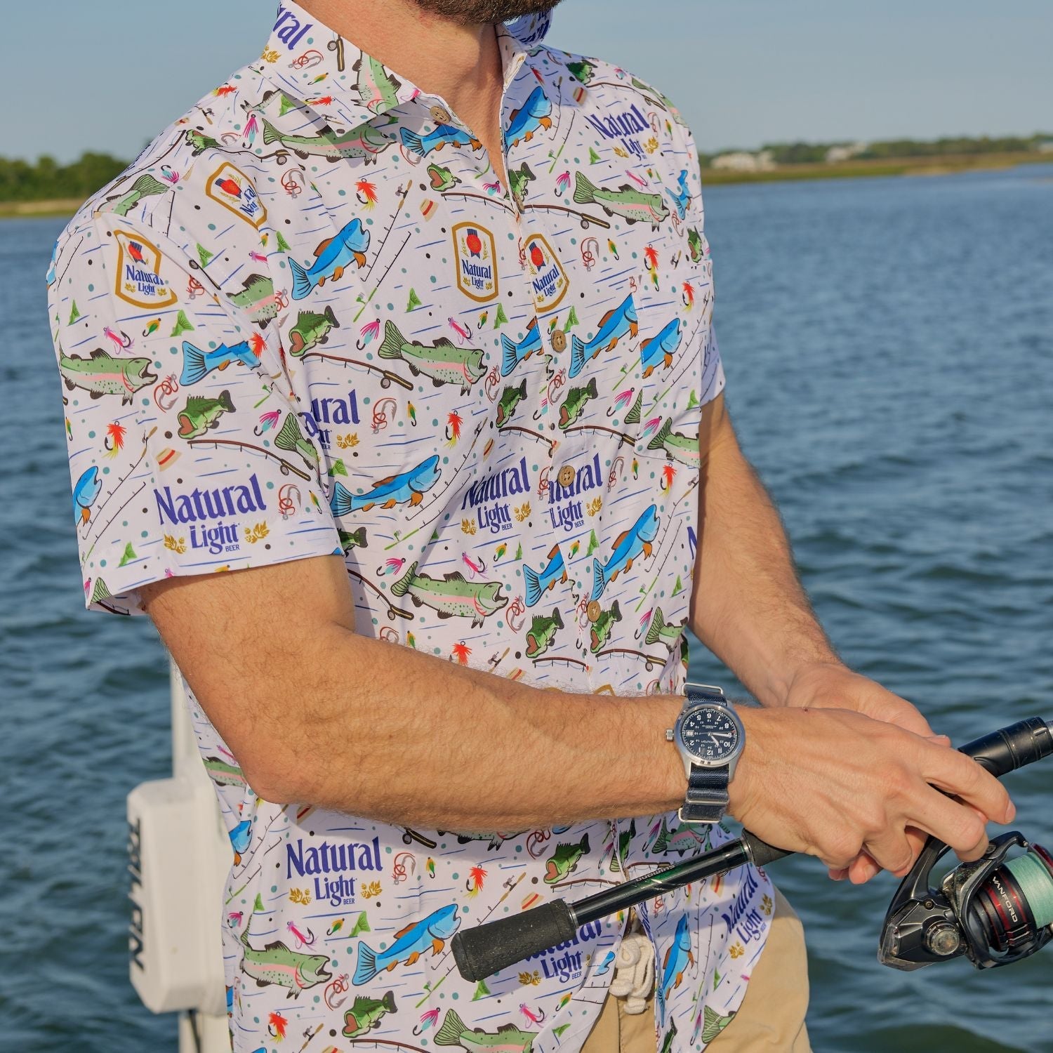 Person wearing a colorful shirt with fishing-themed design by a body of water