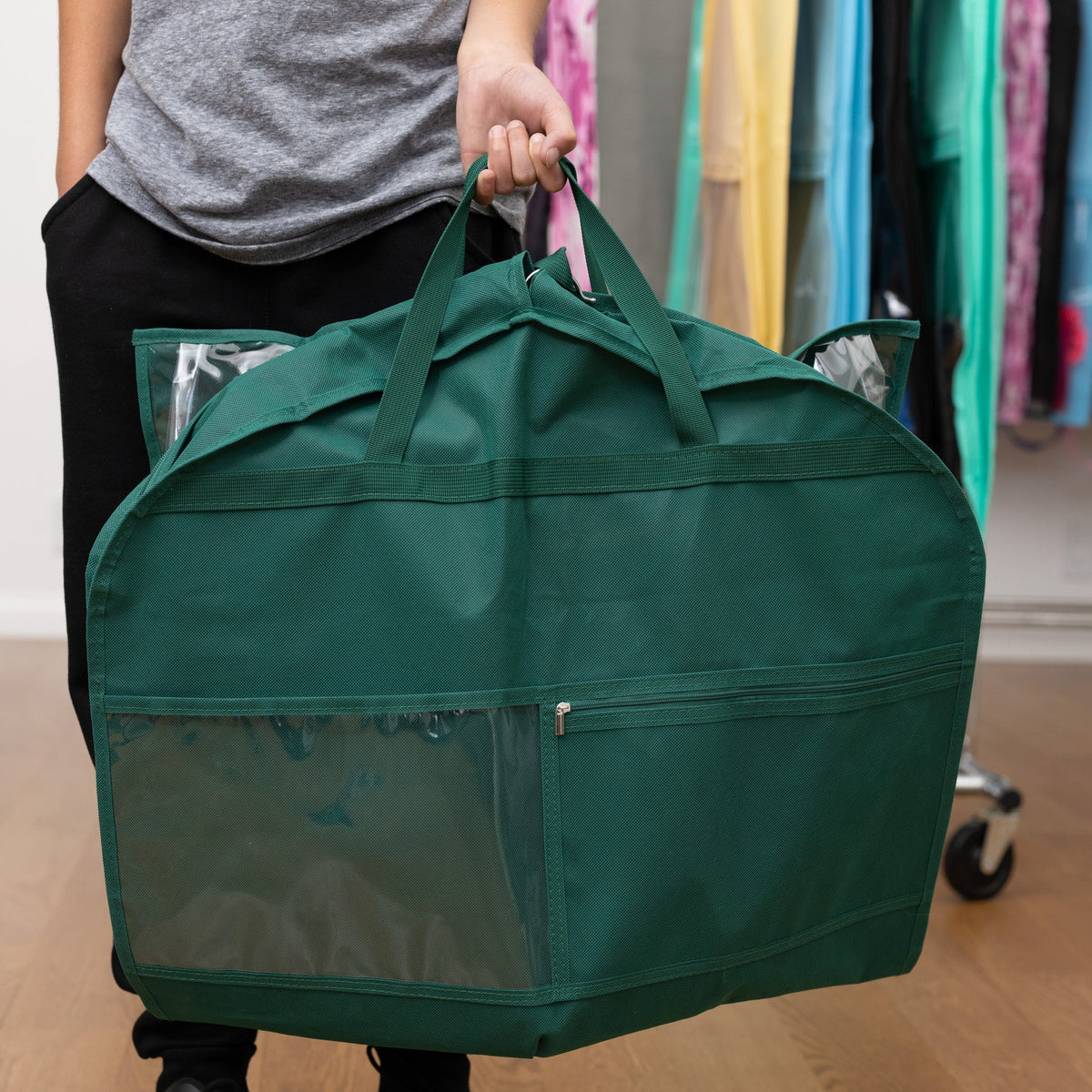 Person holding a green garment bag with clothes inside in a clothing store.