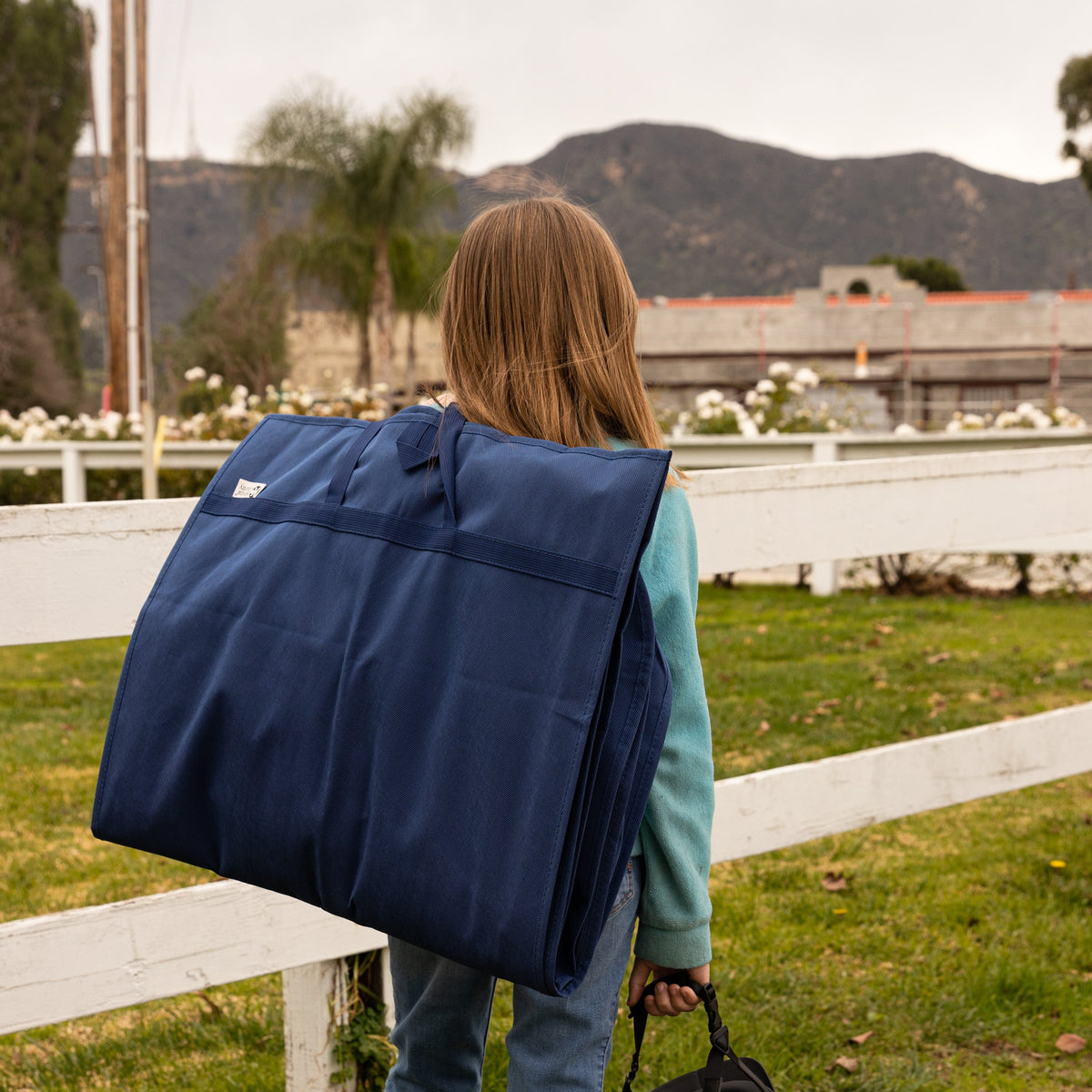 Person carrying a large navy blue bag outdoors with mountains in the background