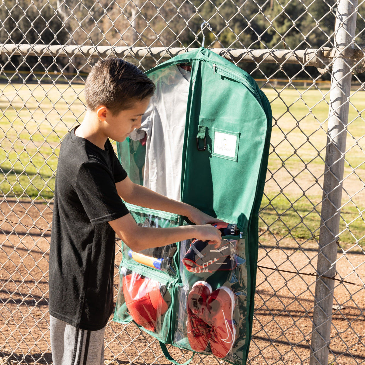 Child using a sports equipment bag outdoors near a chain-link fence.