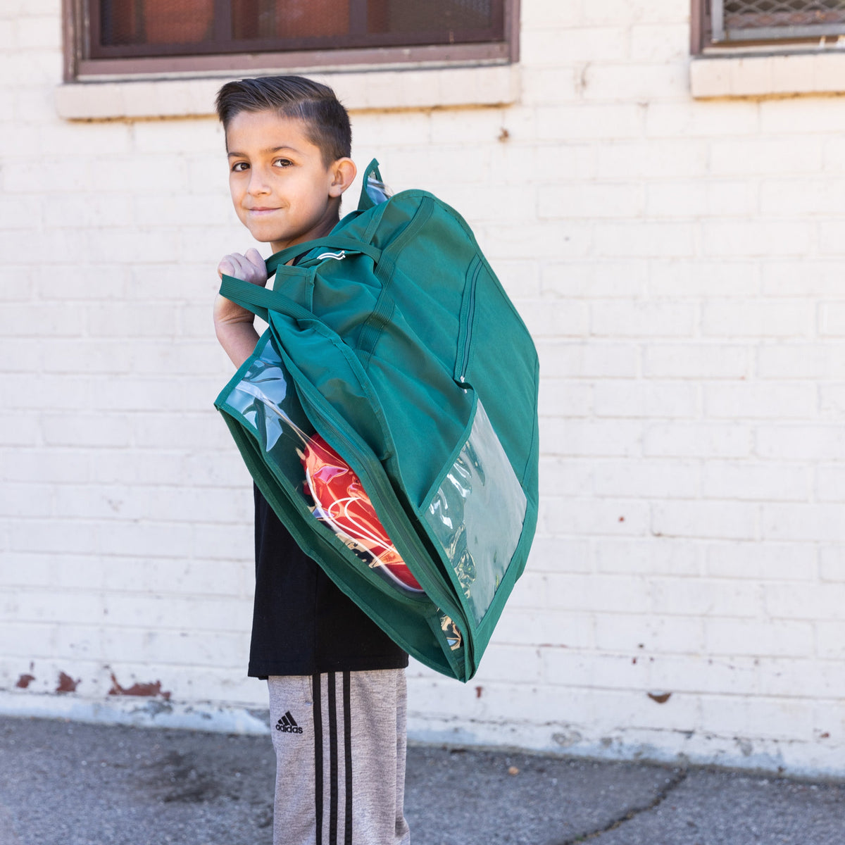 Child holding a green jacket against a white brick wall