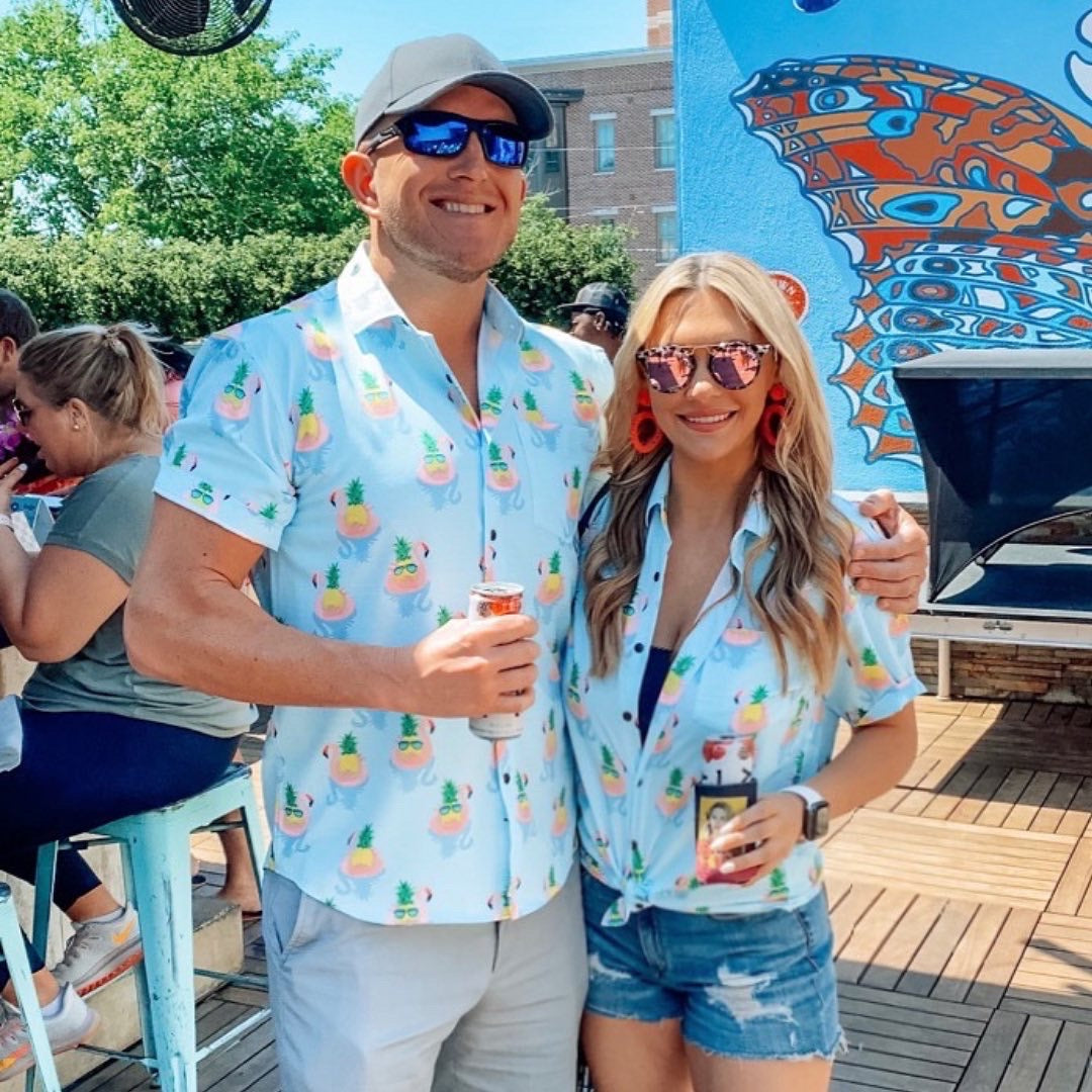 Two people wearing matching light blue shirts with colorful patterns, standing outdoors.